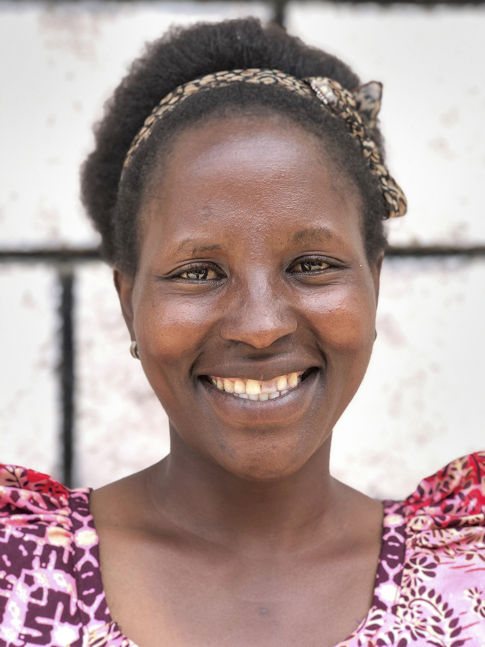 Bildet er et nærbilde av en afrikansk kvinne som smiler mot kamera, hun har kort hår og et hårbånd.