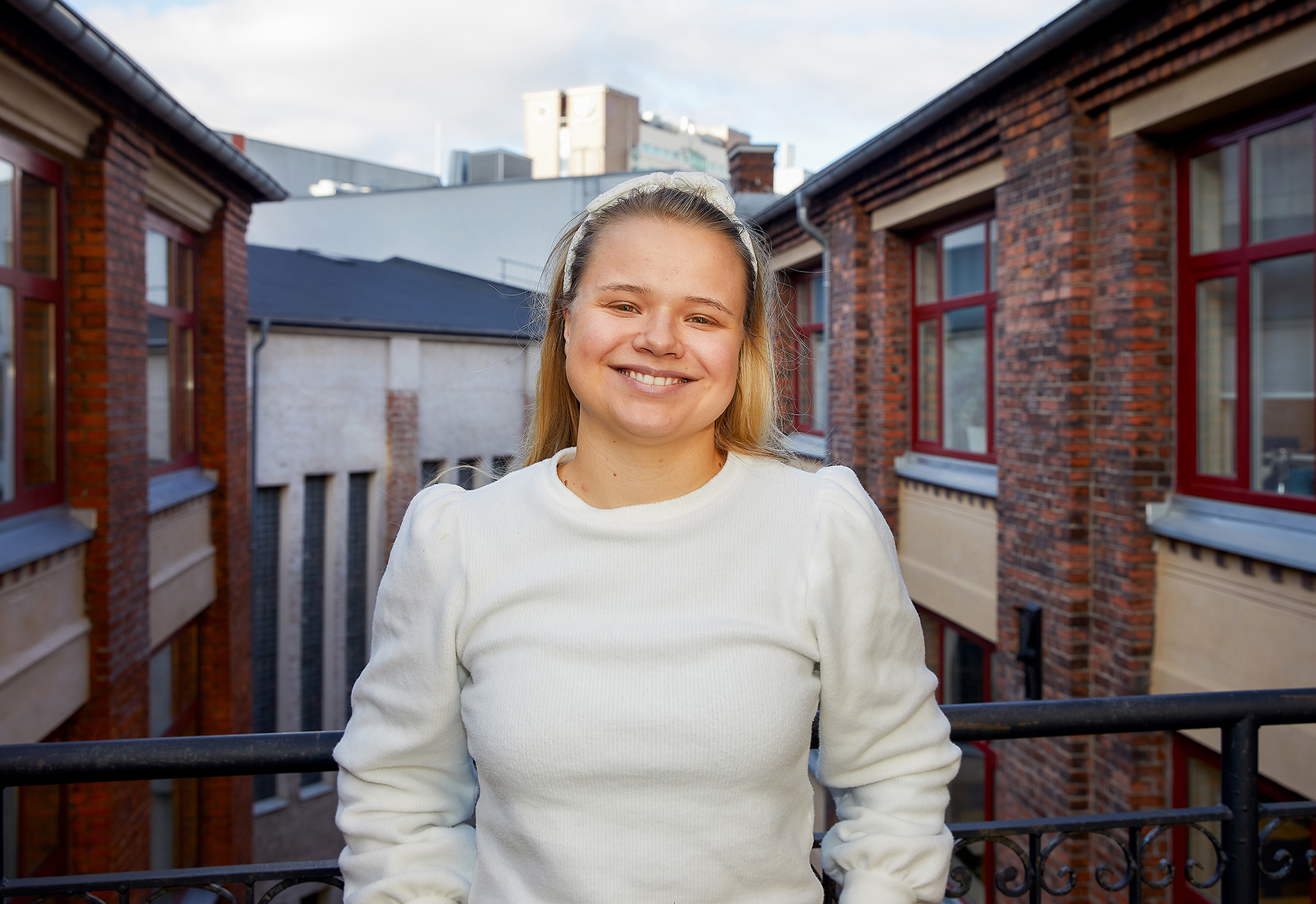 Bildet er et nærbilde av Lisa utendørs, hun står og smiler mot kamera i hvit genser