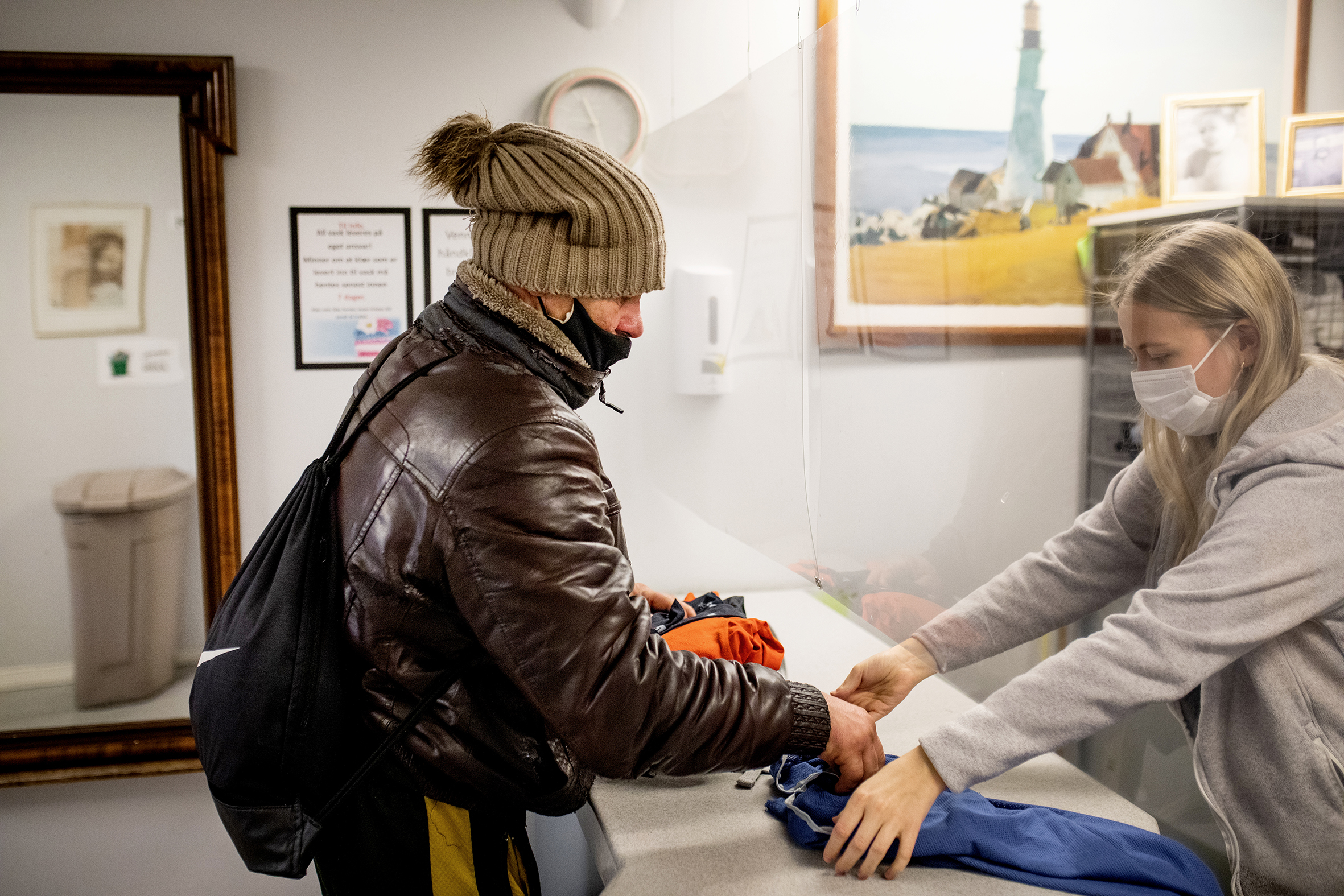 Bilde 1:En dame med yttertøy mottar en pose med klær av en ansatt på Fyrlyset. Begge med munnbind. Bilde 2: 4 skittentøyskurver i ulike farger