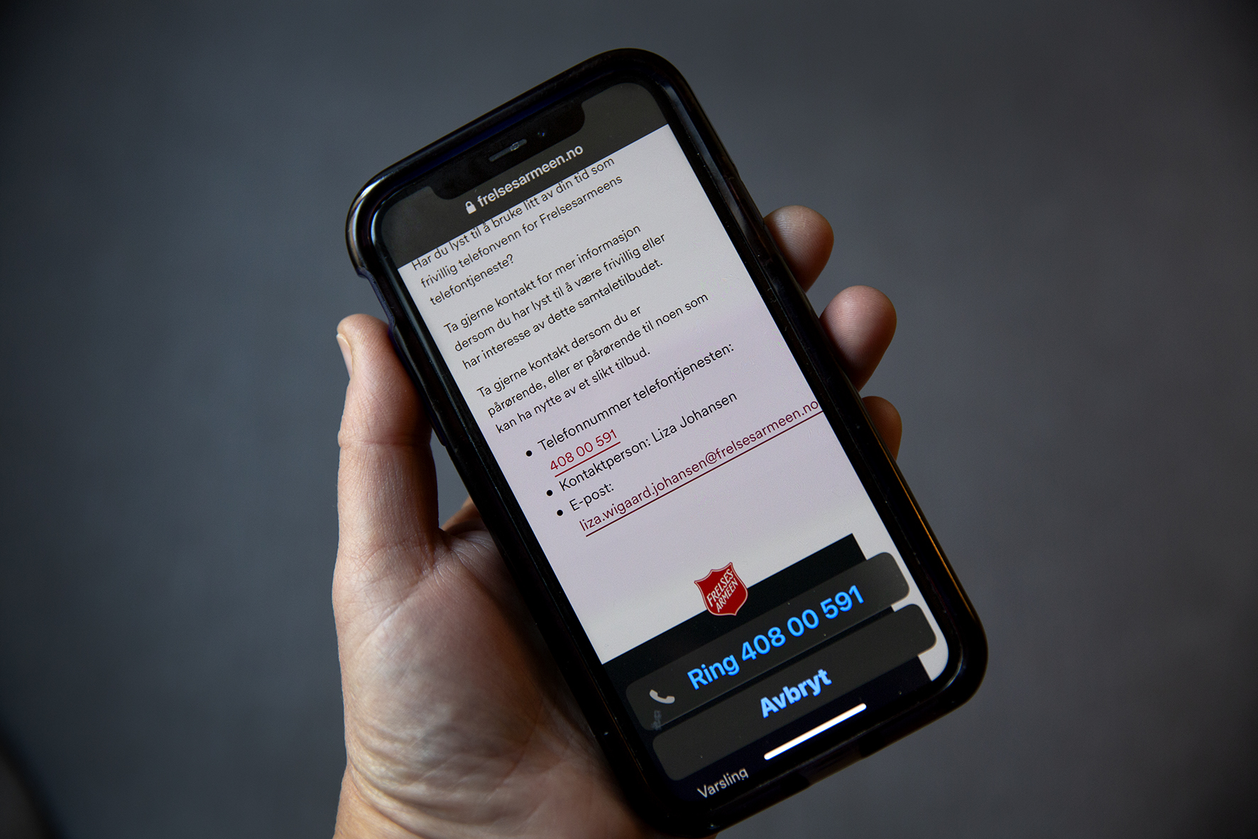 Bilde av en hånd som holder en mobiltelefon som viser nettsiden til Frelsesarmeens telefontjeneste