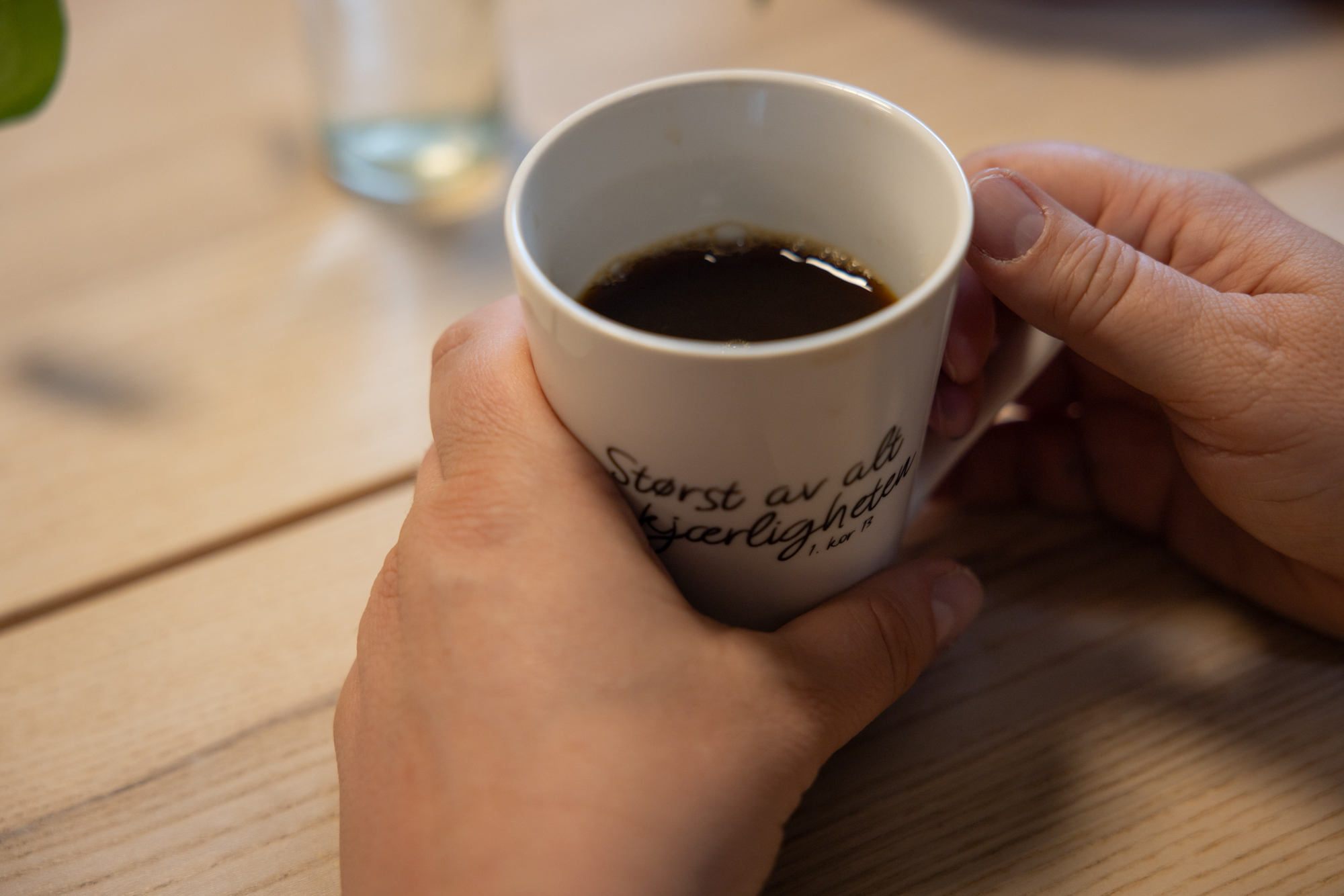 Foto: Nærbilde av hender som holder rundt en hvit kopp med kaffe. På koppen står det "Størst av alt er kjærligheten".