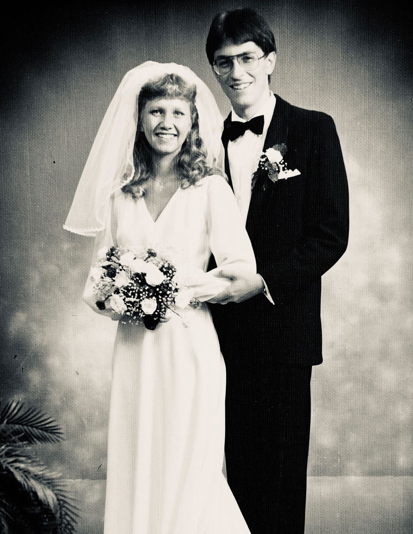 Ungt par i 20-årene, hun blond og i hvit kjole med bukett og han i mørk dress og bruker briller.