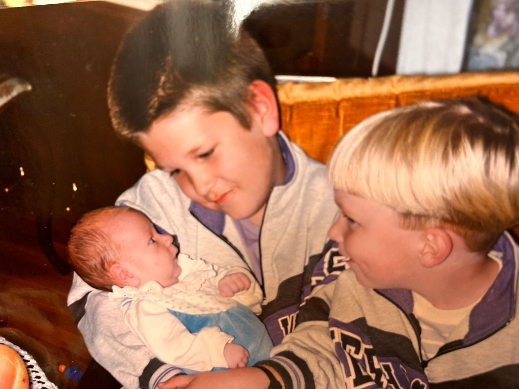 To brødre, en mørk og en blond, sitter i sofaen med en nyfødt babybror. Det er på 1990-tallet.