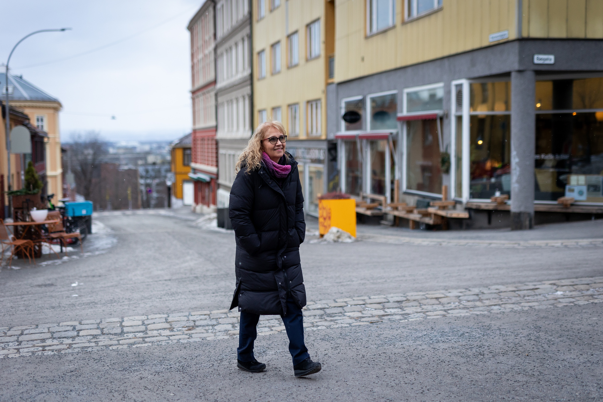 Foto: Kvinne i boblekåpe går i en bygate på toppen av en bakke med utsikt over byen.