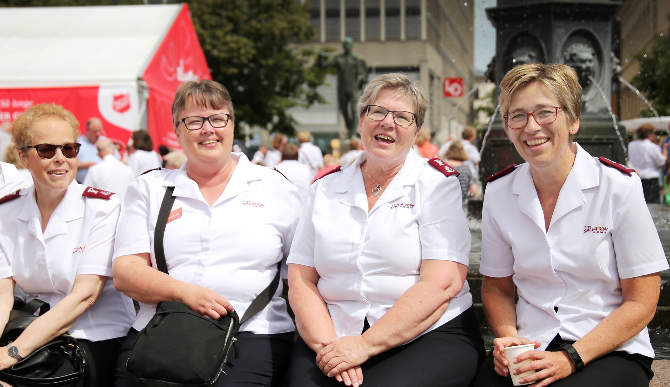 4 kvinner sittende i uniform smilende i sola