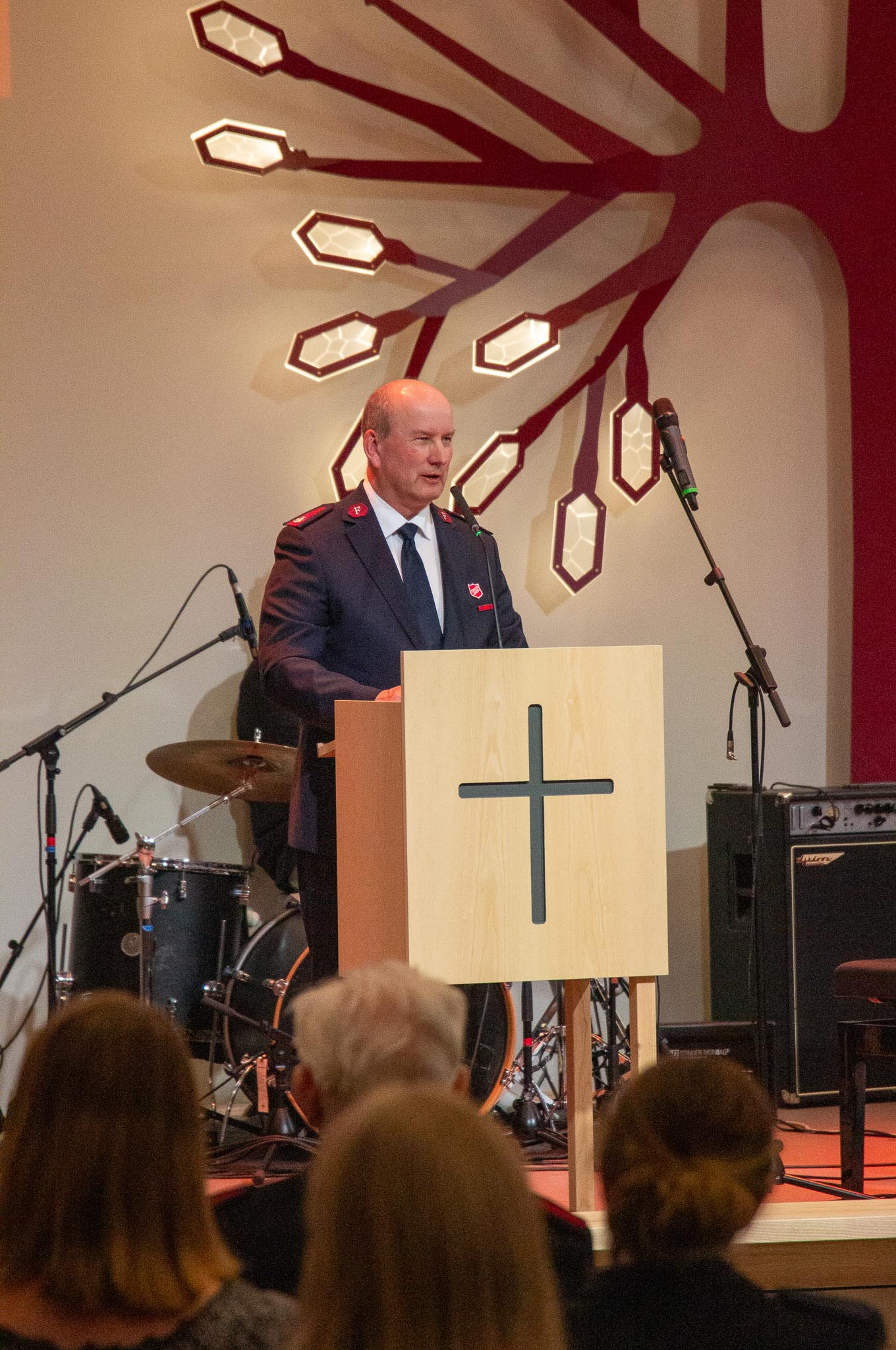Rektor ved Offisersskolen, major Tom Kristiansen står på et podium foran en trehvit talerstol med kors på. Han har på uniform og har majors rang.