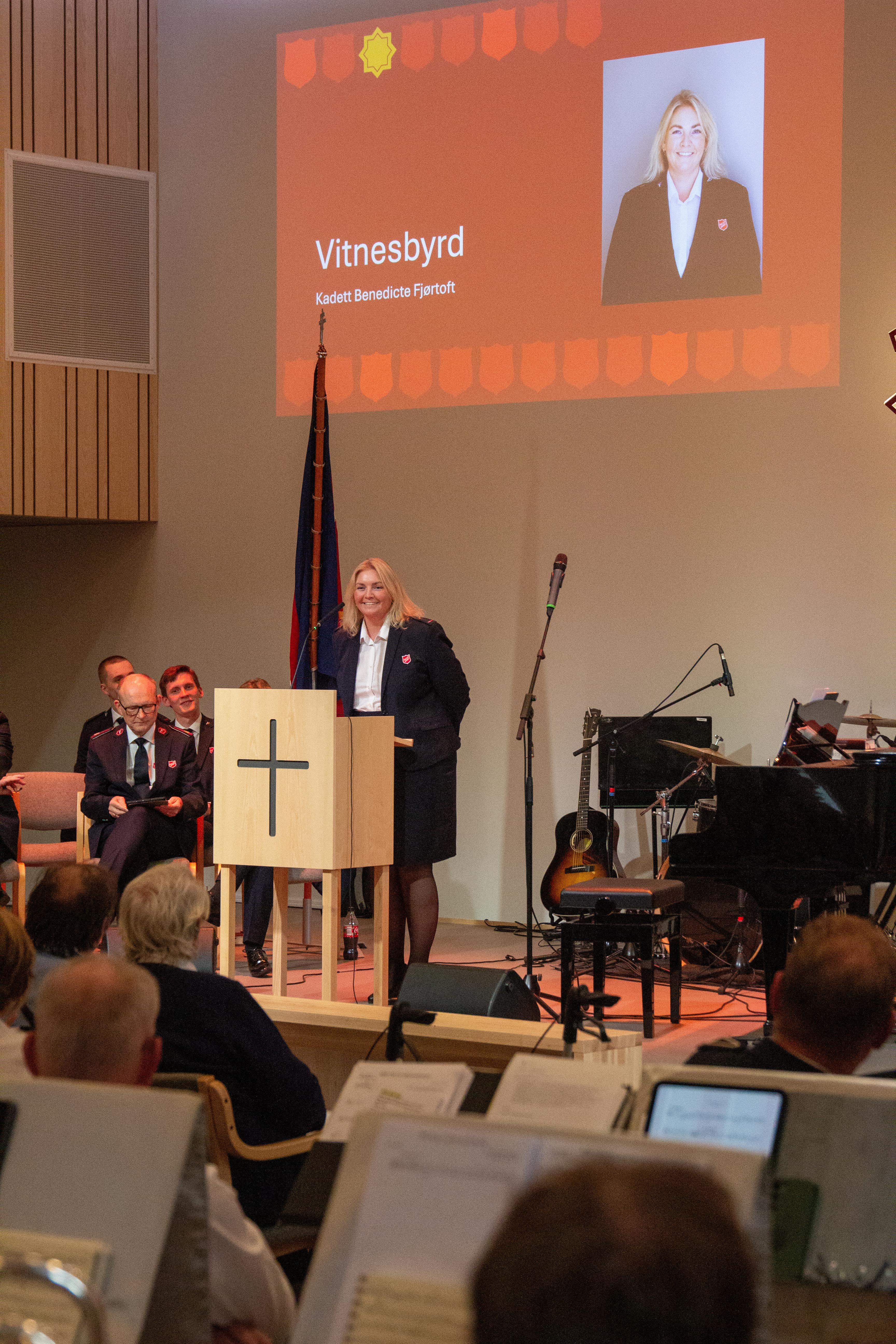 Benedicte Fjørtoft står bak en talerstol på Ensjø korps. Hun holder et vitnesbyrd.