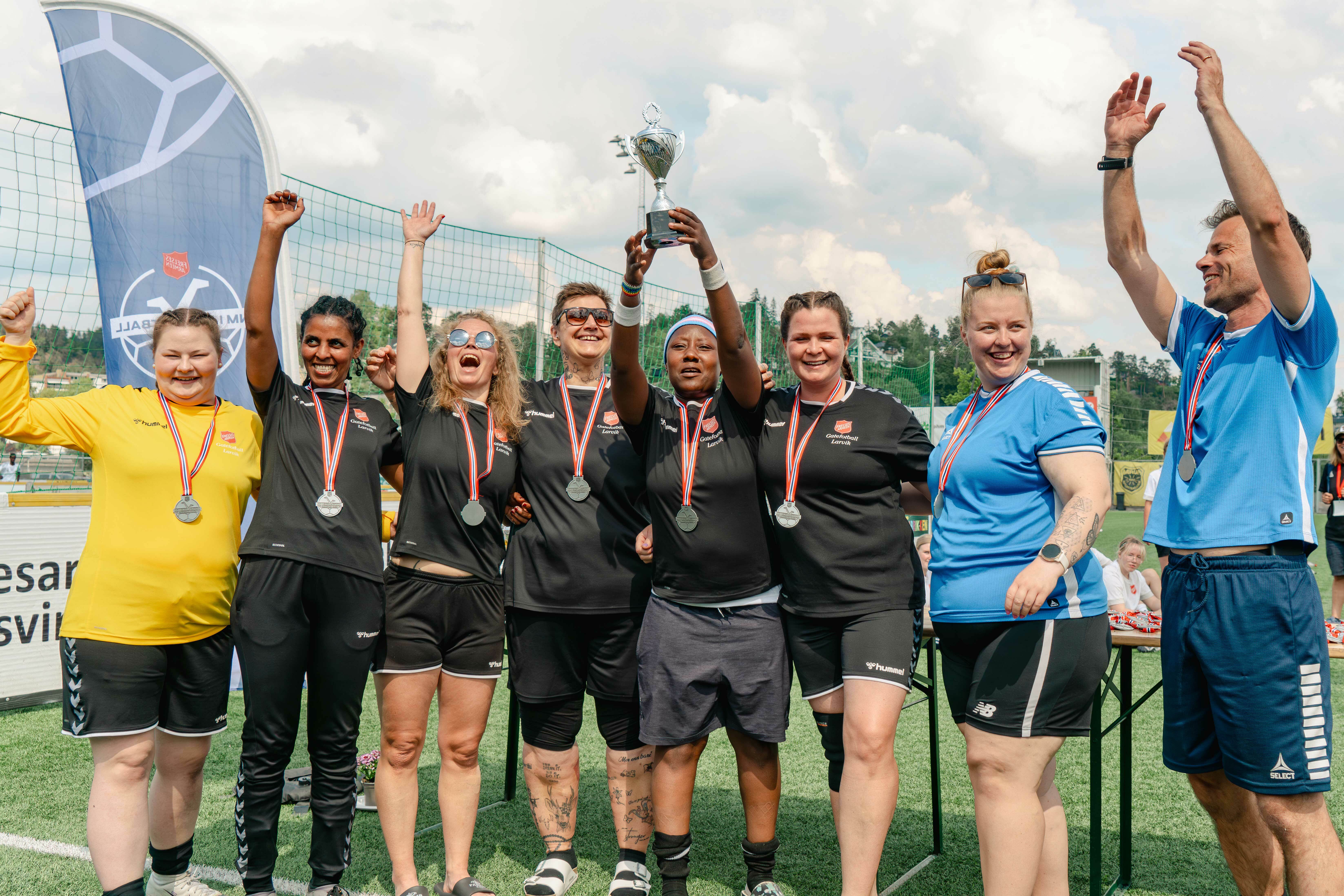 Kvinnelige fotballspillere som strekker hendene i været på en fotballbane. Treneren til høyre.
