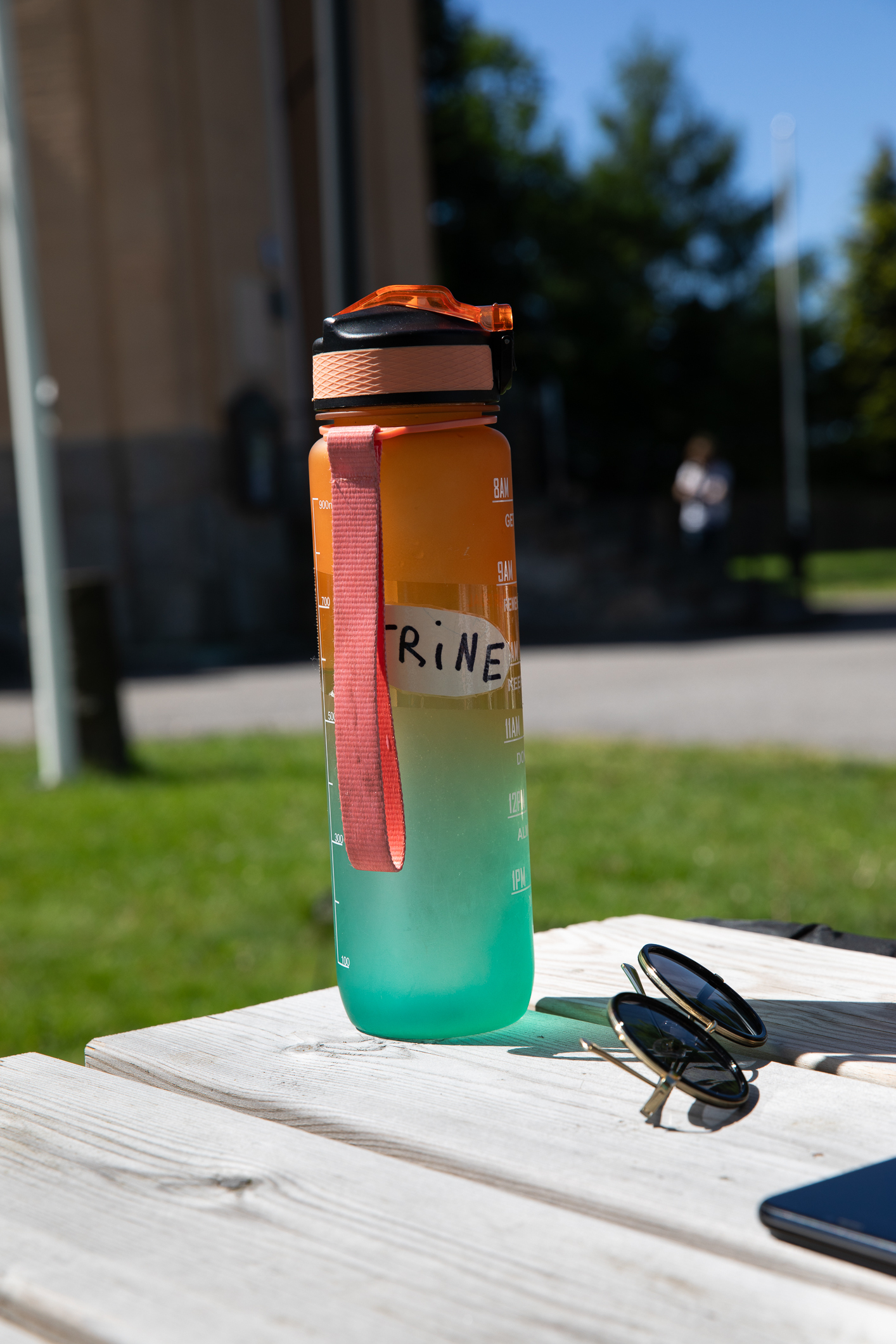 Vannflaske med navnet trine på og solbriller på et utebord