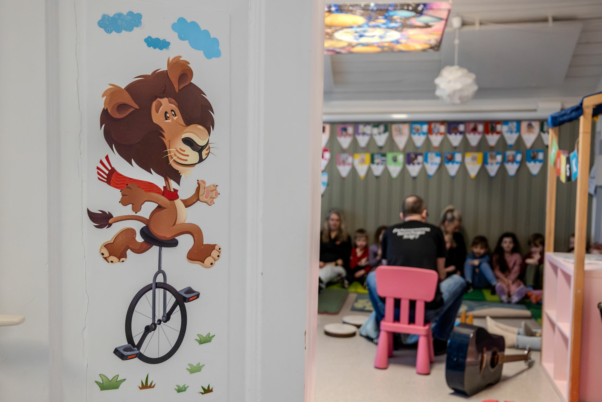 Foto: En gammel, hvitmalt dør står på gløtt og der inne sitter en barnehageonkel på en liten stol og forteller eventyr til barna.