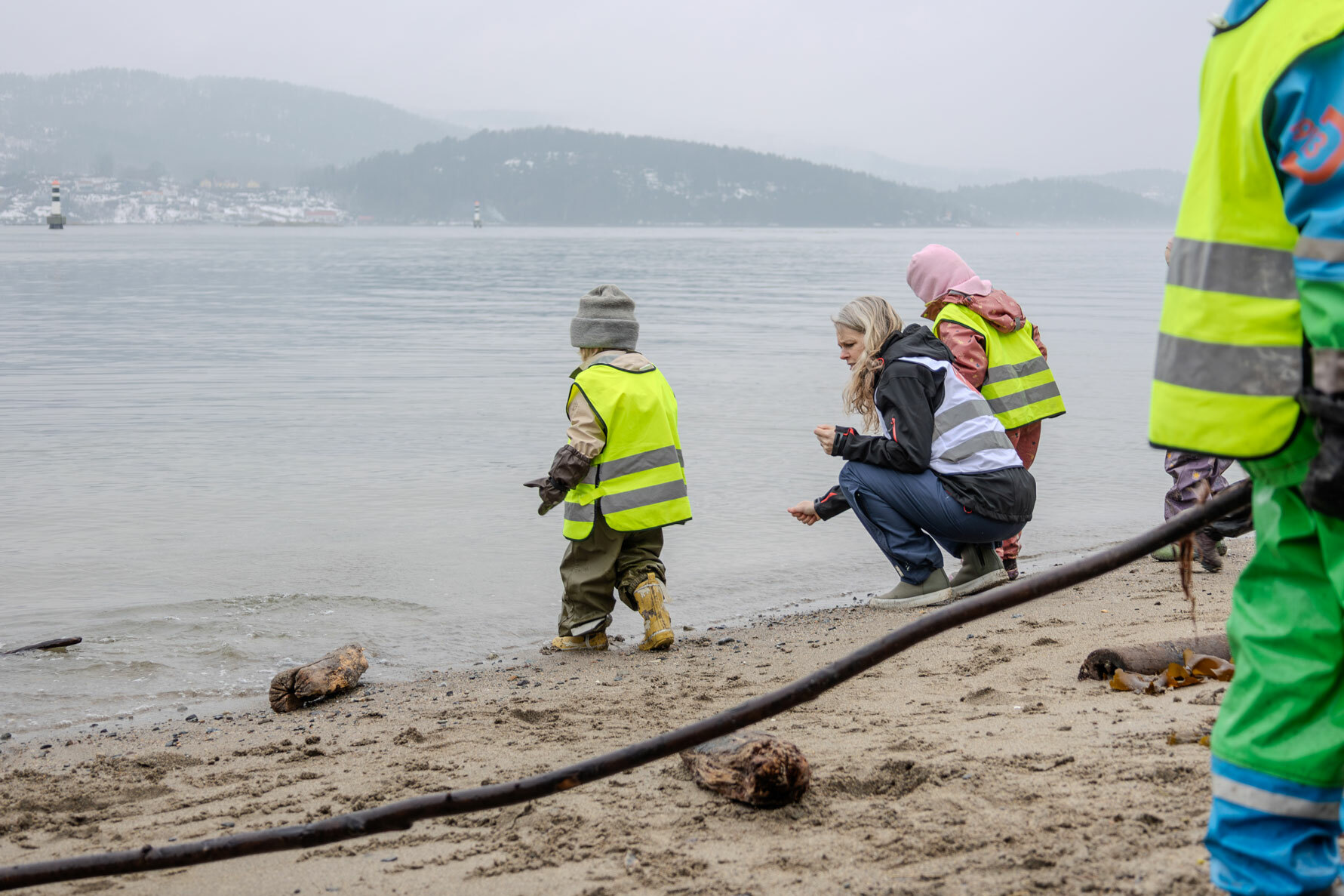 Foto: To bildere etter hverandre der det første viser en gjeng med barnehagebarn og to ledere som går langs en vei. De har på seg refleksvester. Det andre bildet viser dem leke i de samme vestene på en sandstarnd ved sjøen.
