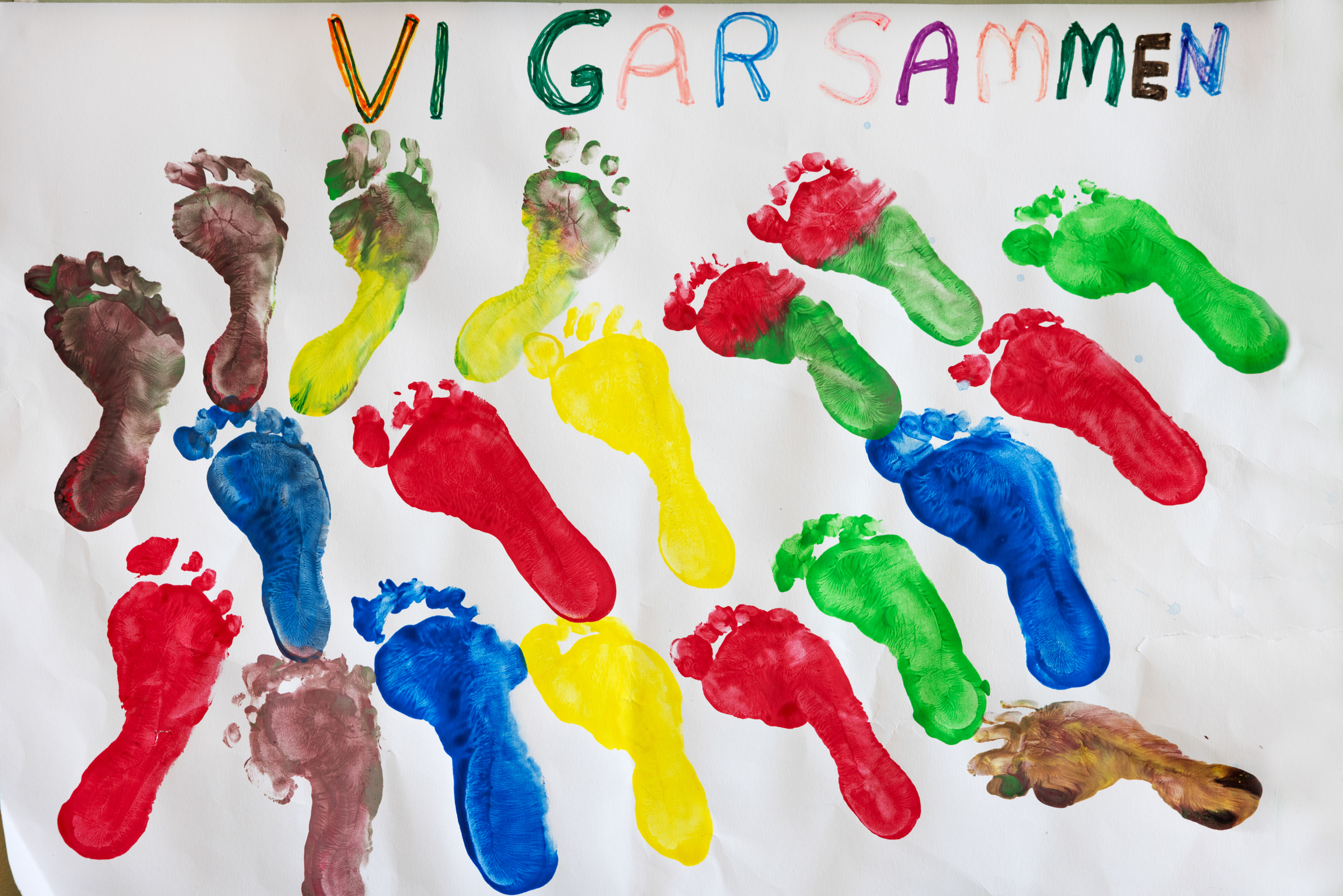 Hvitt ark med trykk fra mange barneføtter. Over står det: Vi går sammen.