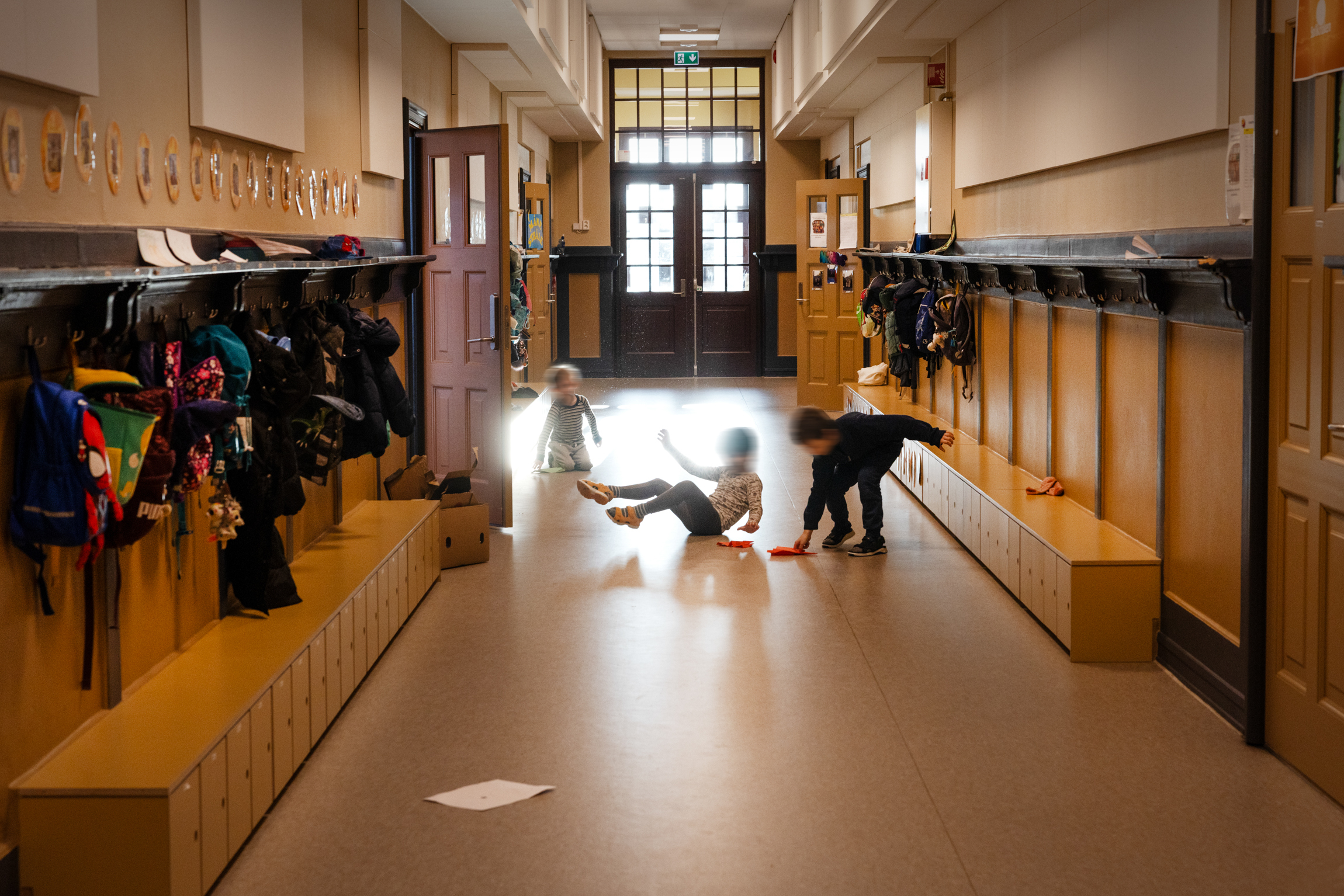 Tre barn som leker seg i en stor gang med knaggrekker og uteklær.