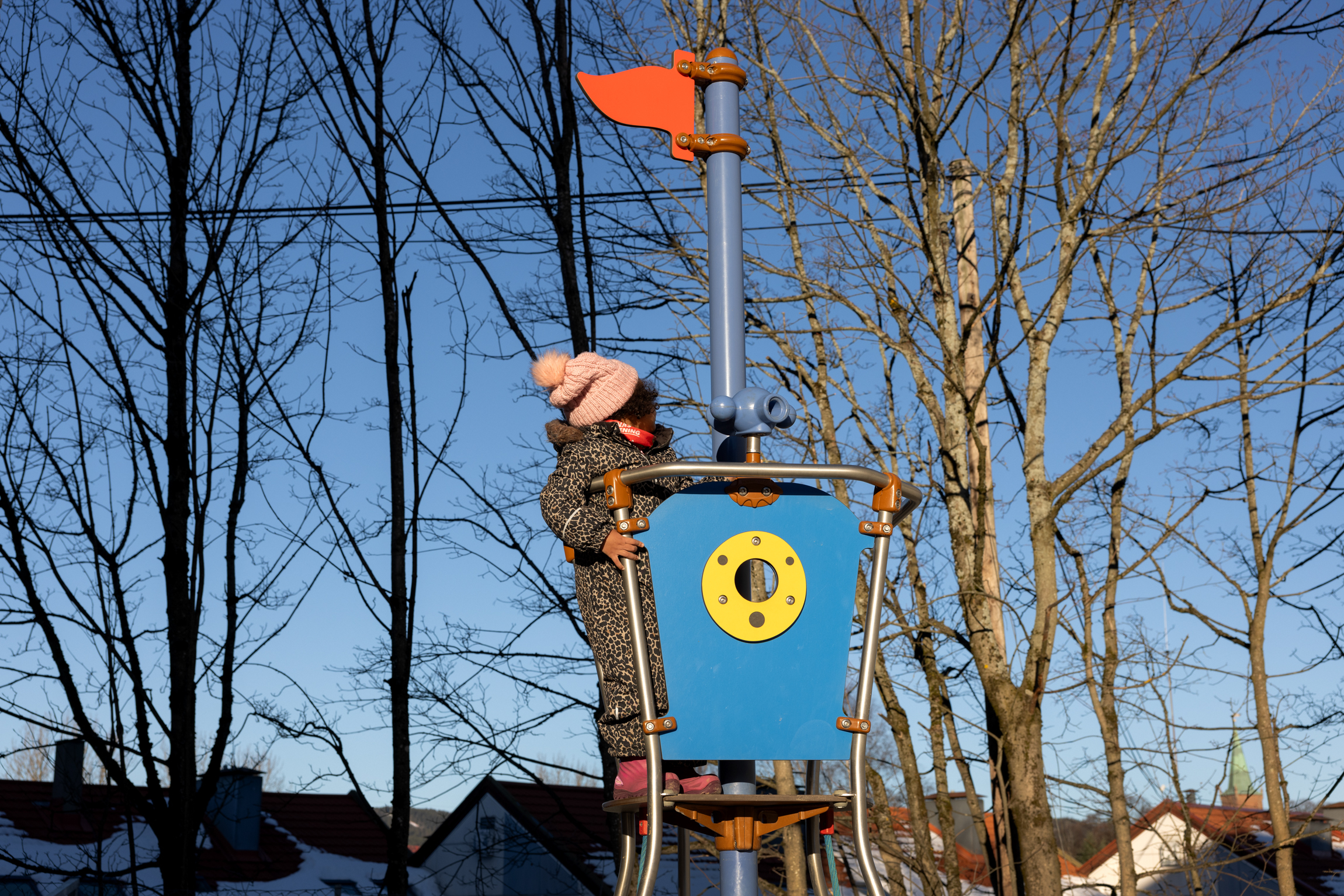 Jente i vinterdress skuer utover fra et leketårn med flagg på toppen.