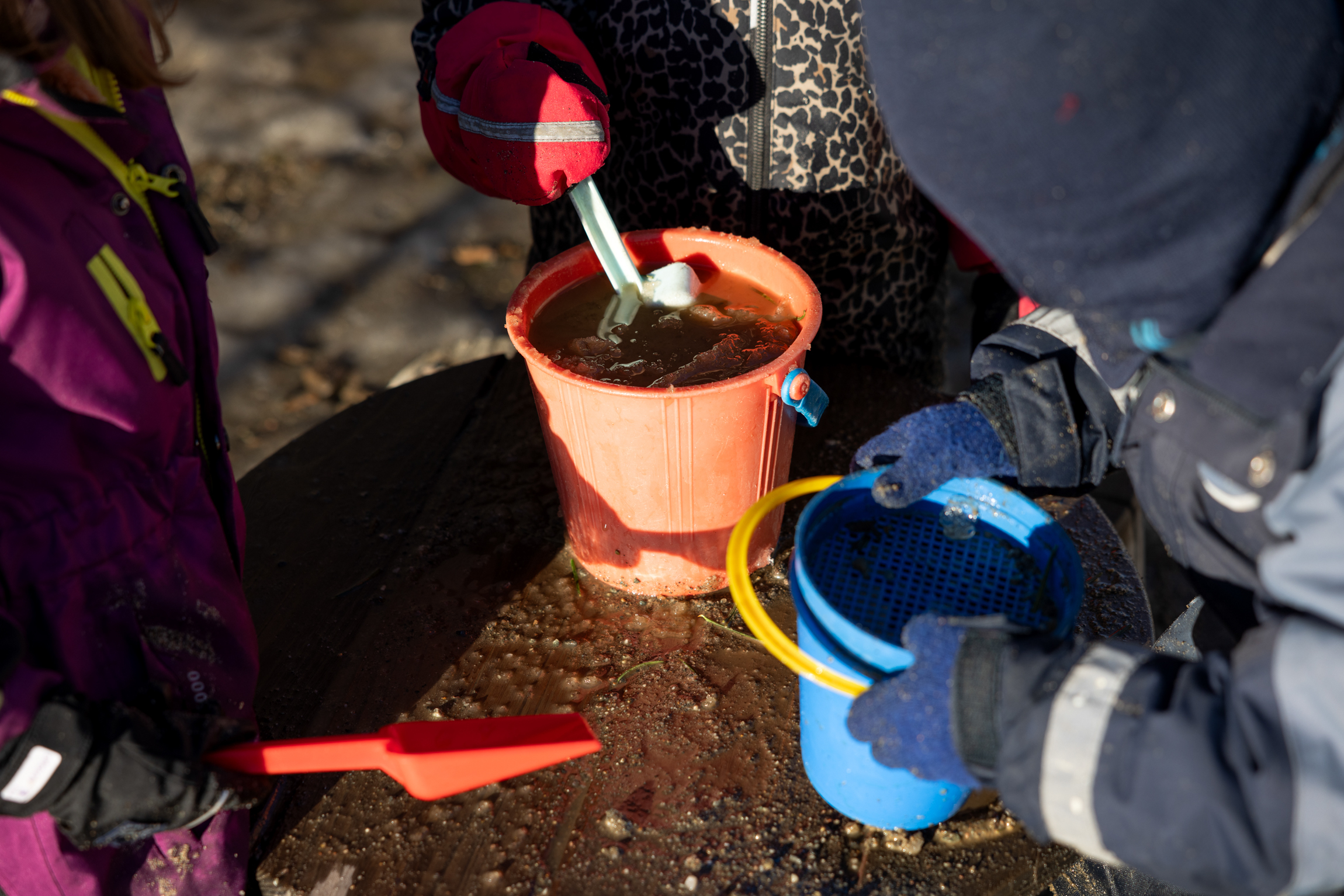 To bilder som begge viser barnehender som leker i sandkassen
