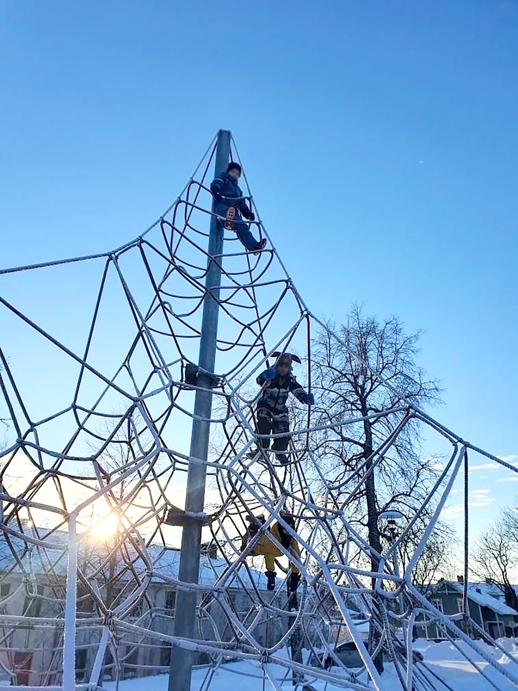 Tre barn oppe i et stort klatrestativ om vinteren.
