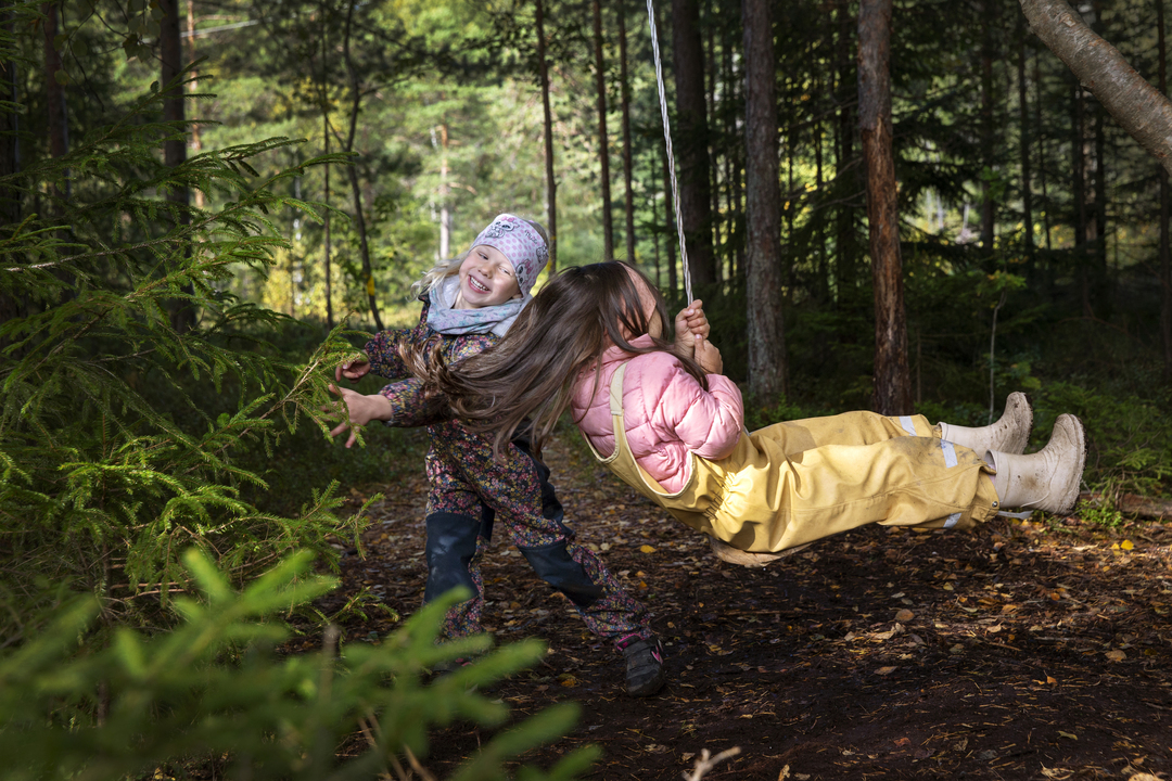 Foto: To bilder etter hverandre der det første viser en jente som henger i et tau og en annen jente som ler ved siden av henne. Det andre bildet er av de samme to jentene og tre andre barn som løper rundt en gammel, høy trestubbe.