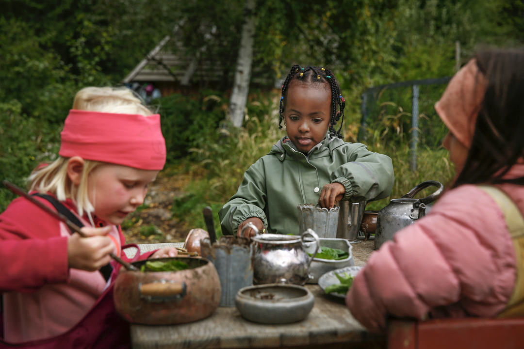 Foto: To bilder etter hverandre der det første viser tre jenter som sitter ved et trebord ute. De har dekket på med "mat" de har rørt sammen. Det andre er et nærbilde av denne "maten" som serveres.
