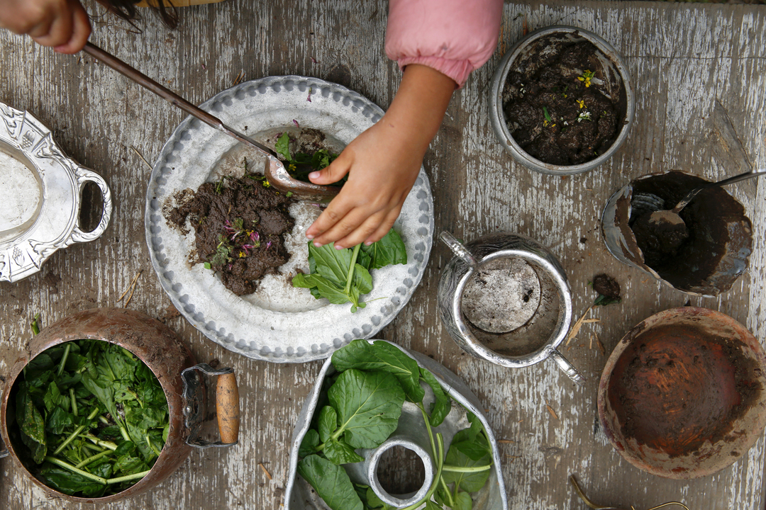 Foto: To bilder etter hverandre der det første viser tre jenter som sitter ved et trebord ute. De har dekket på med "mat" de har rørt sammen. Det andre er et nærbilde av denne "maten" som serveres.