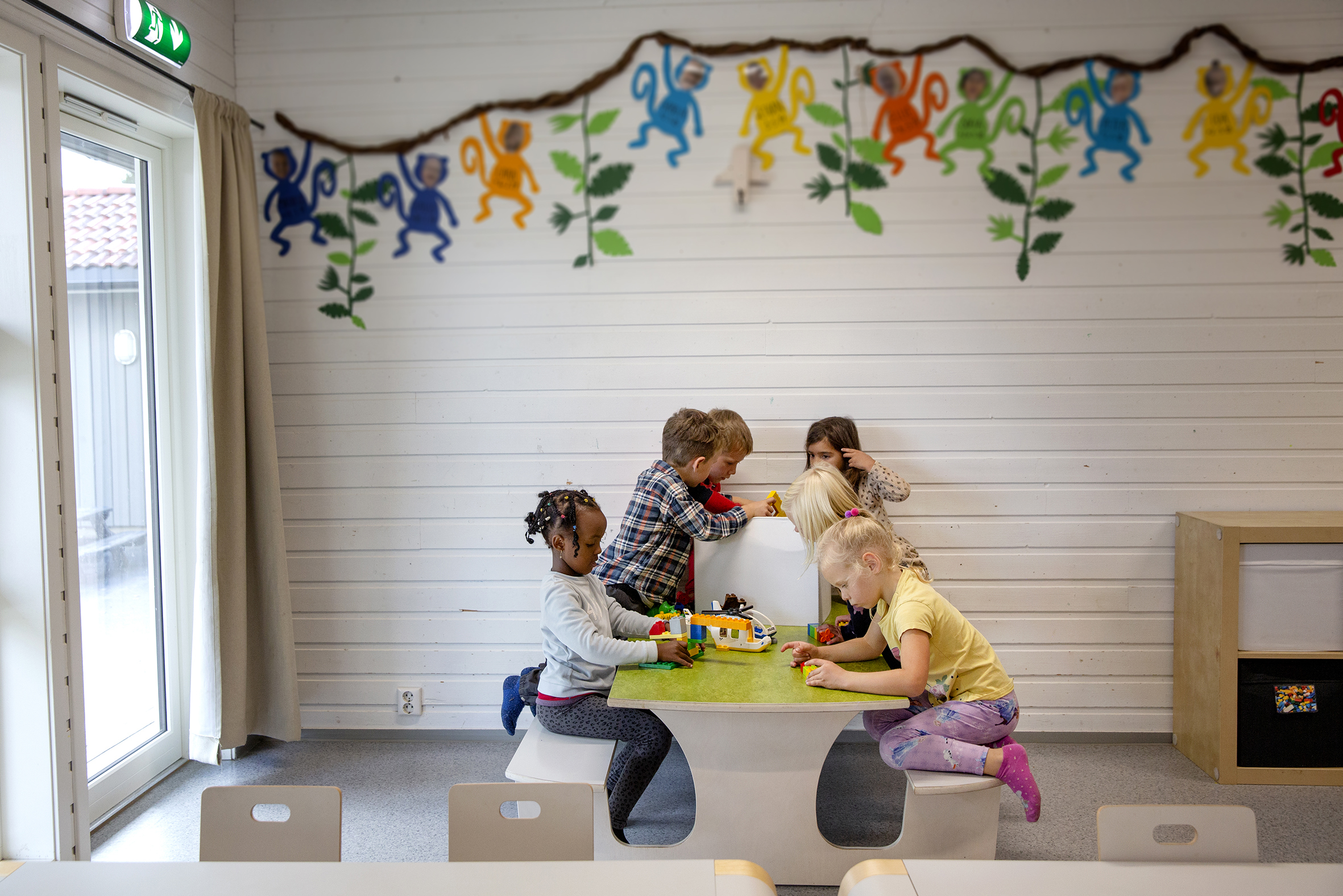 Foto: Seks barnehagebarn sitter rolig ved et bord og leker sammen. De bygger ting.