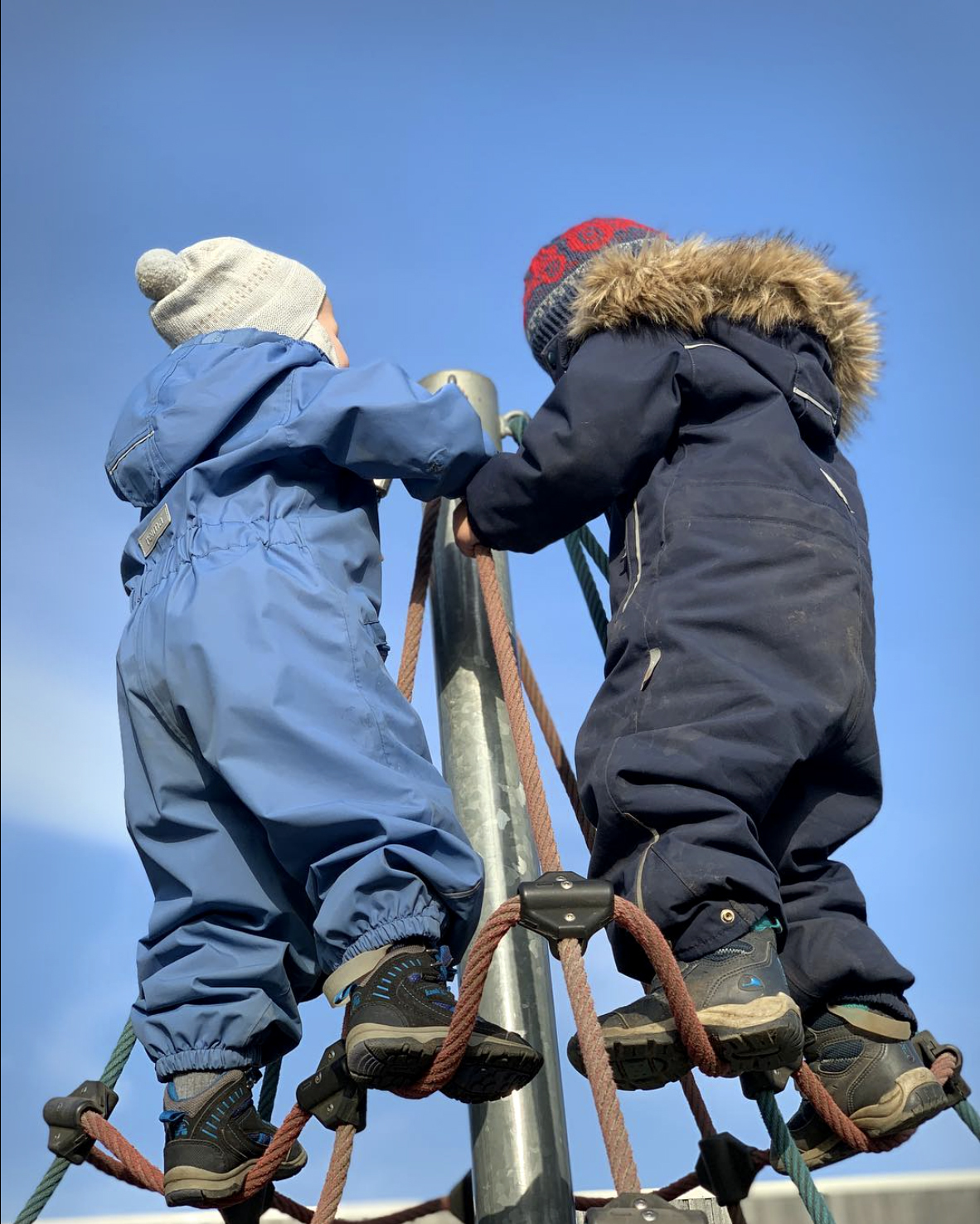 Foto: To gutter i 4-5-årsalder står i toppen av et lekestativ med netting. De har ryggen mot kamera.