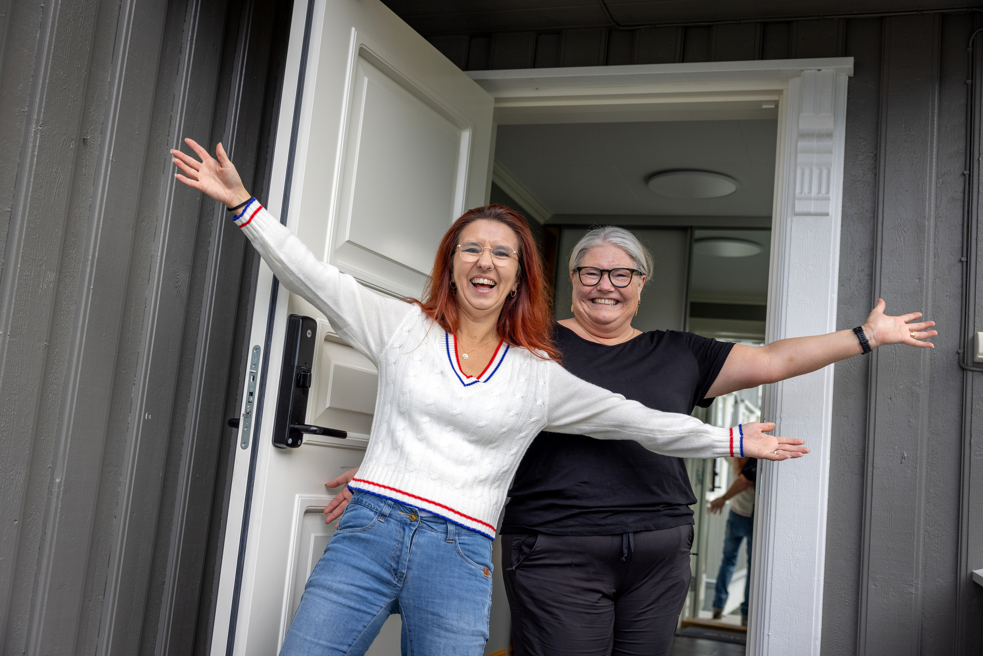 Foto: To kvinner står i en døråpning med armene strakt ut i et velkommen!