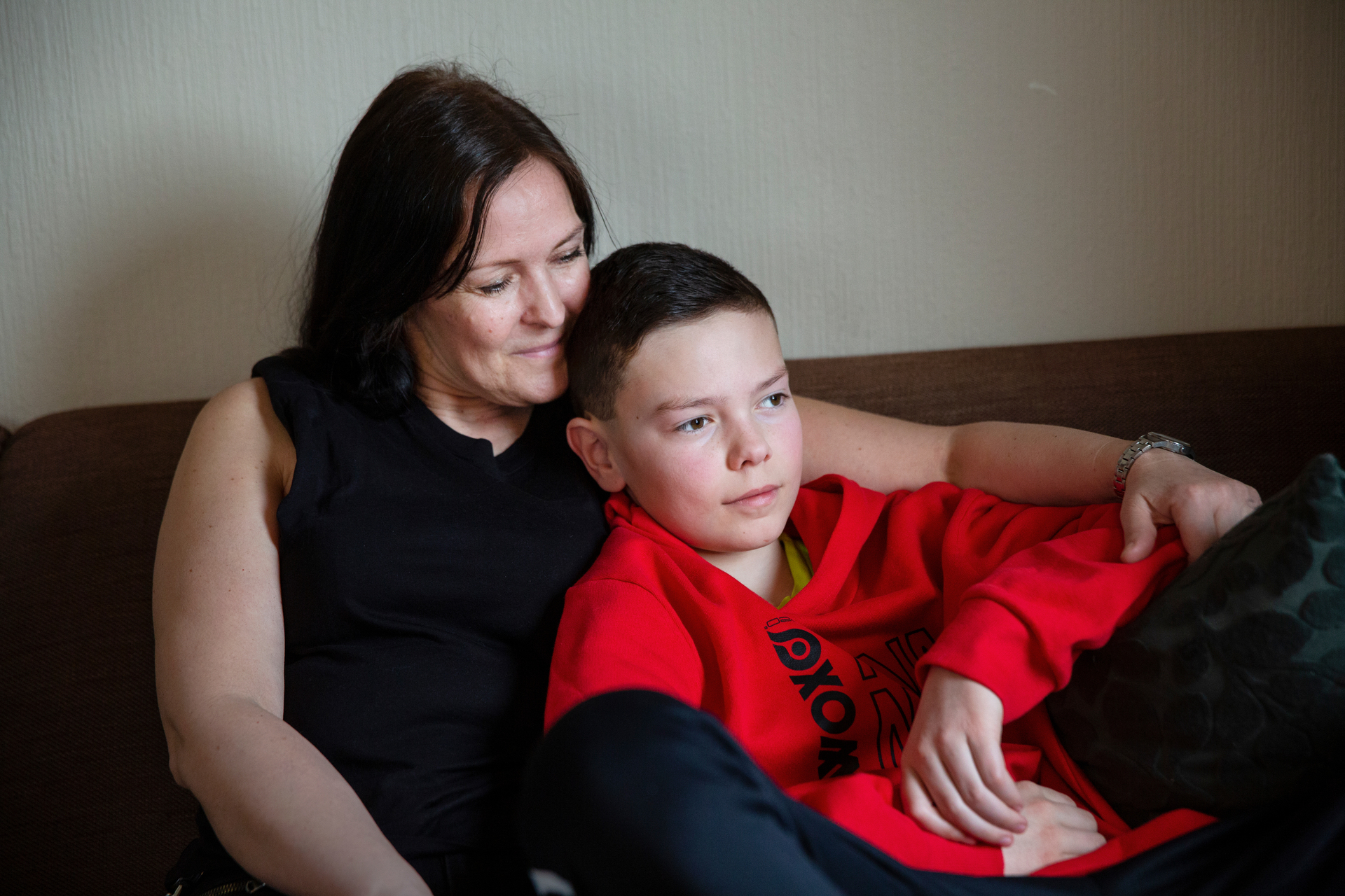 Foto: Kvinne sitter i en sofa. I armkroken sitter en gutt på rundt 12 år.