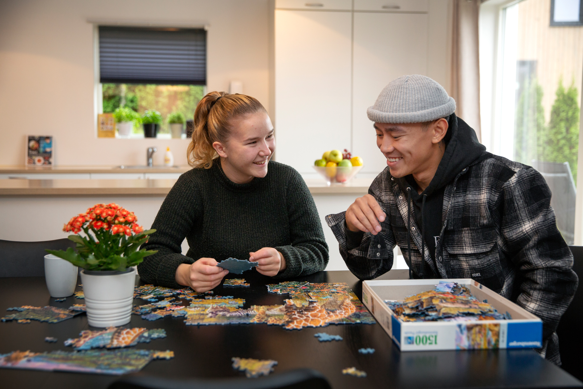 Foto: Ung mann og tenåringsjente legger puslespill på kjøkkenet.