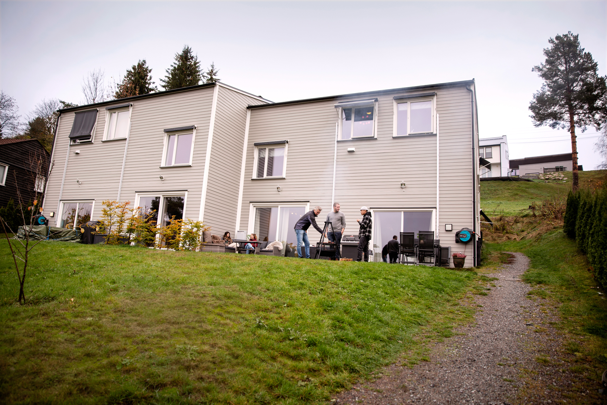 Foto: To grå, moderne tomannsboliger ligger i en skråning med grønn plen foran.