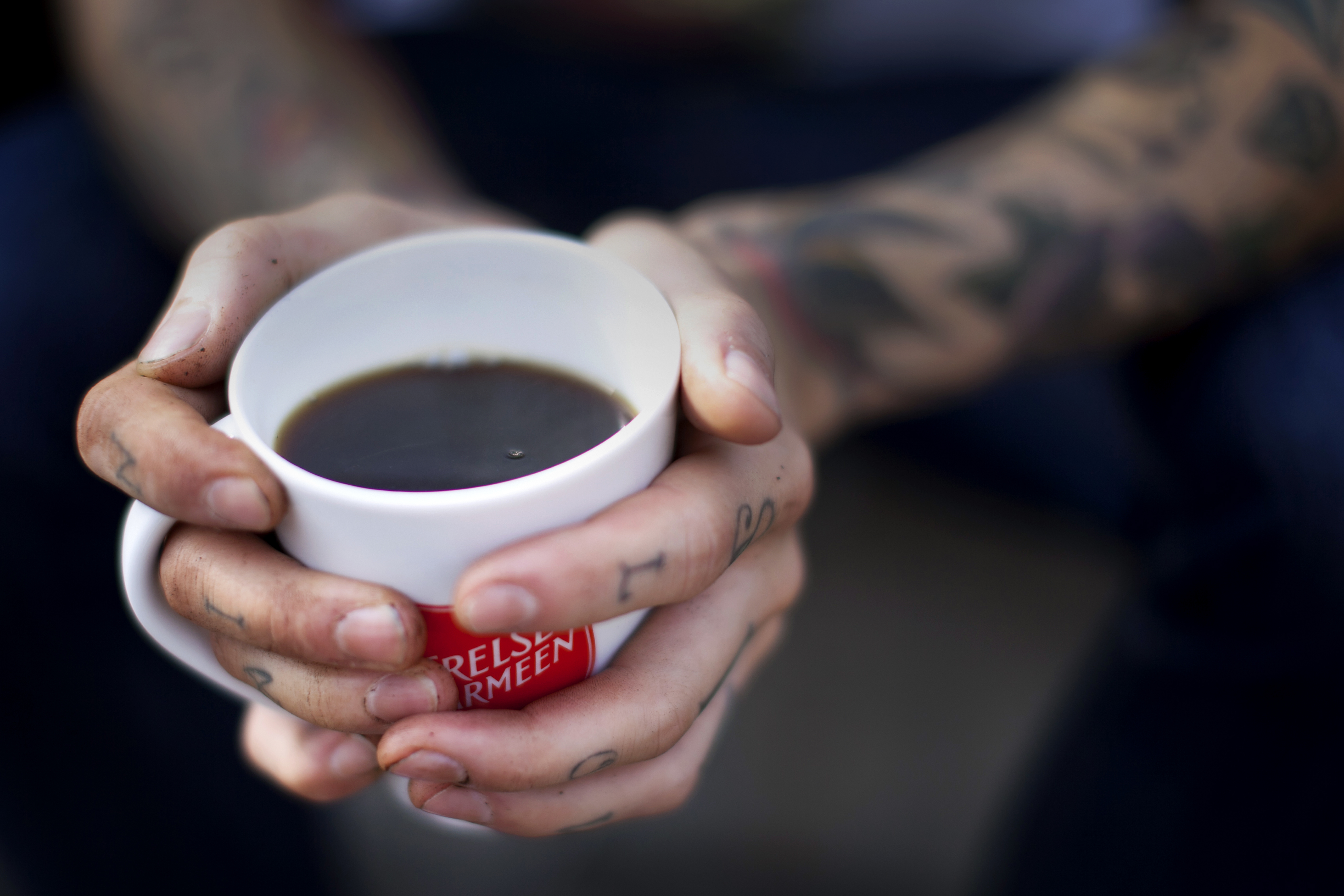 Tatoverte hender holder kopp med skjold