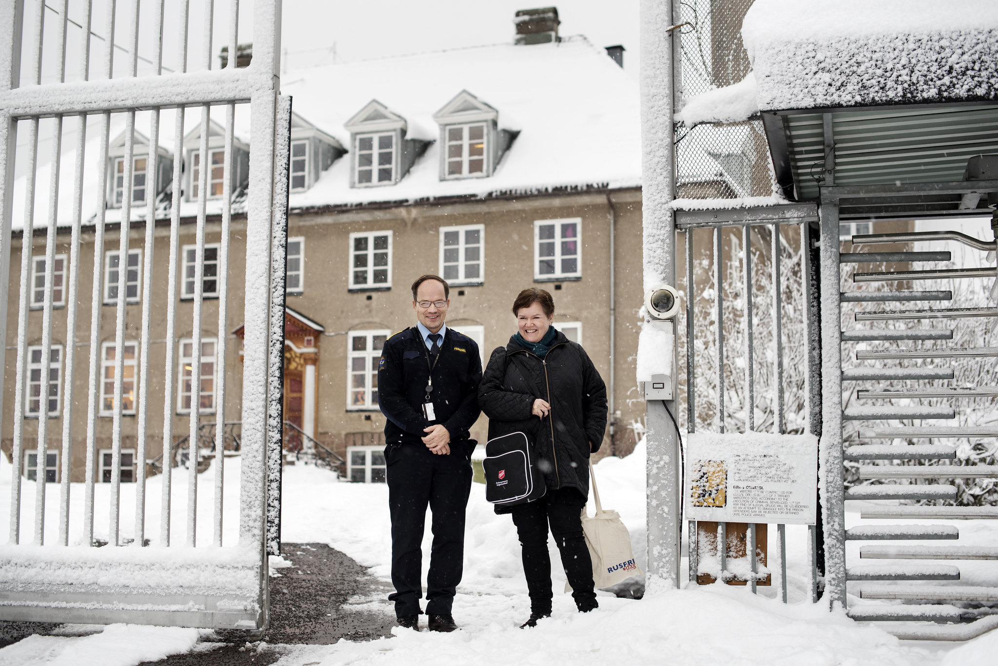 Dame fra Frelsesarmeen og uniformert mann står ved inngangsporten til et fengsel.