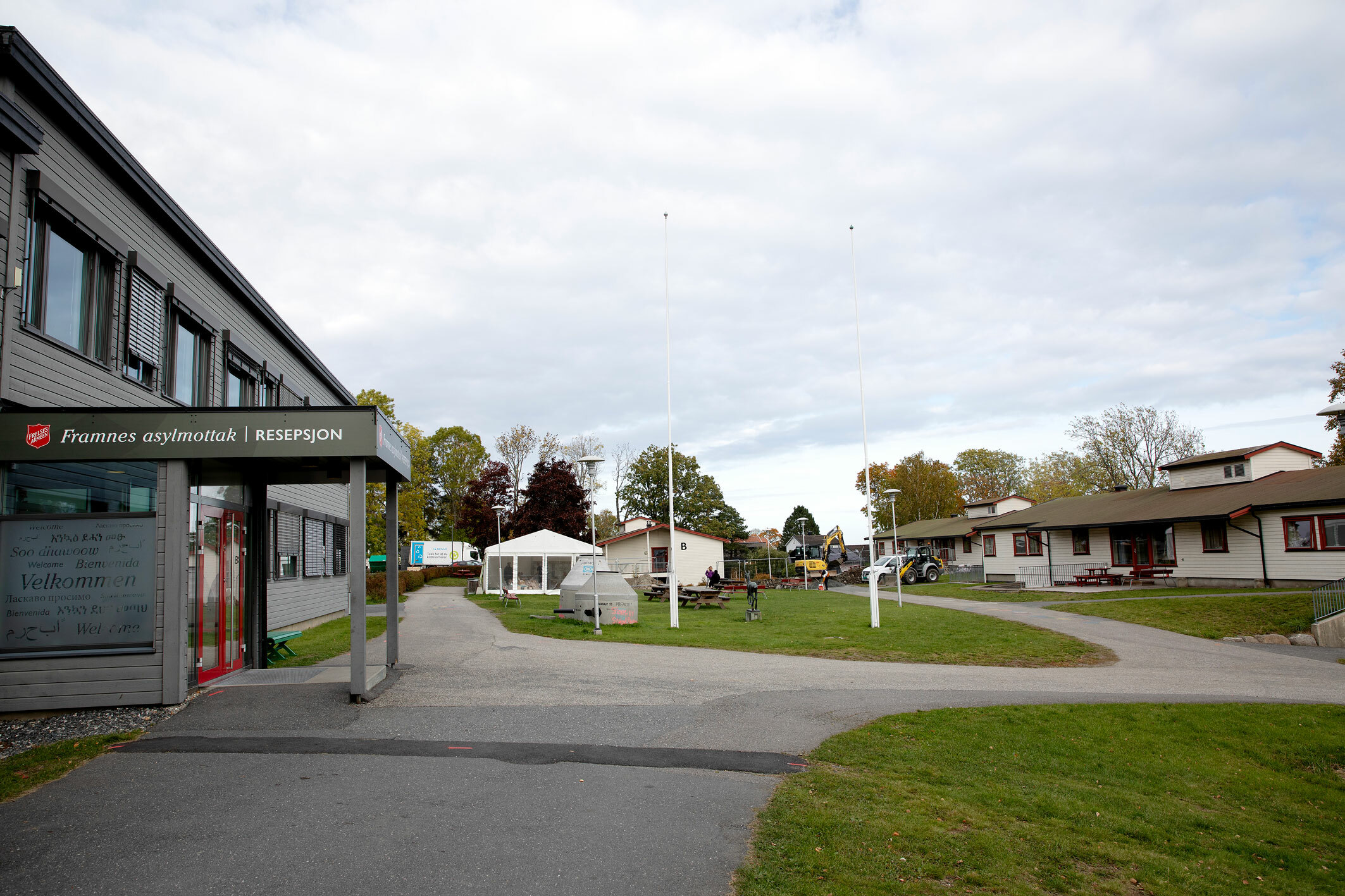 Foto: Til venstre et stort, toetasjes grått bygg i tre. Ellers er det lavere bygg rundt det.