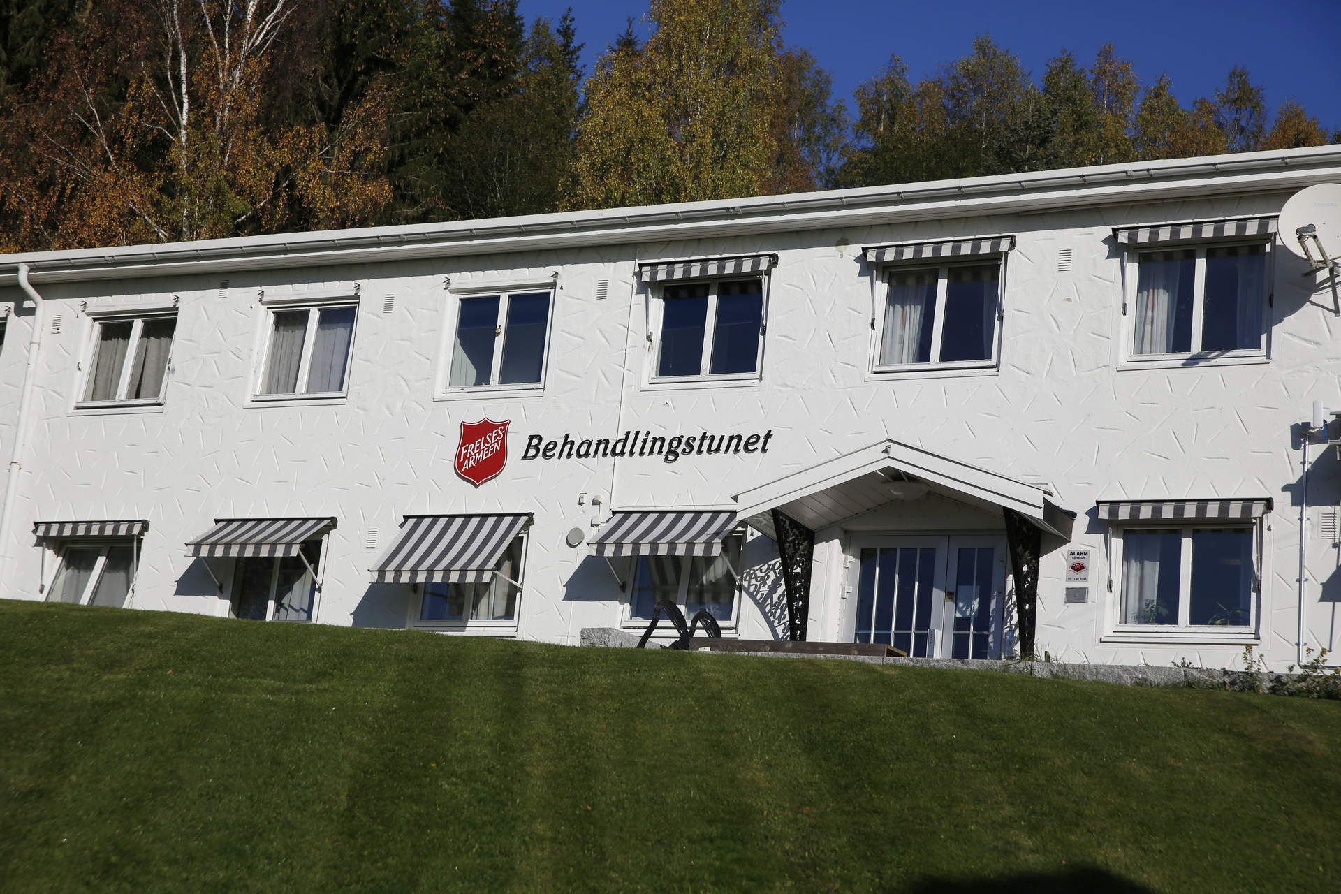 Foto: Bilde av hvitt, avlangt murbygg i to etasjer der det står Behandlingstunet i store bokstaver, men Frelsesarmeens logo foran.