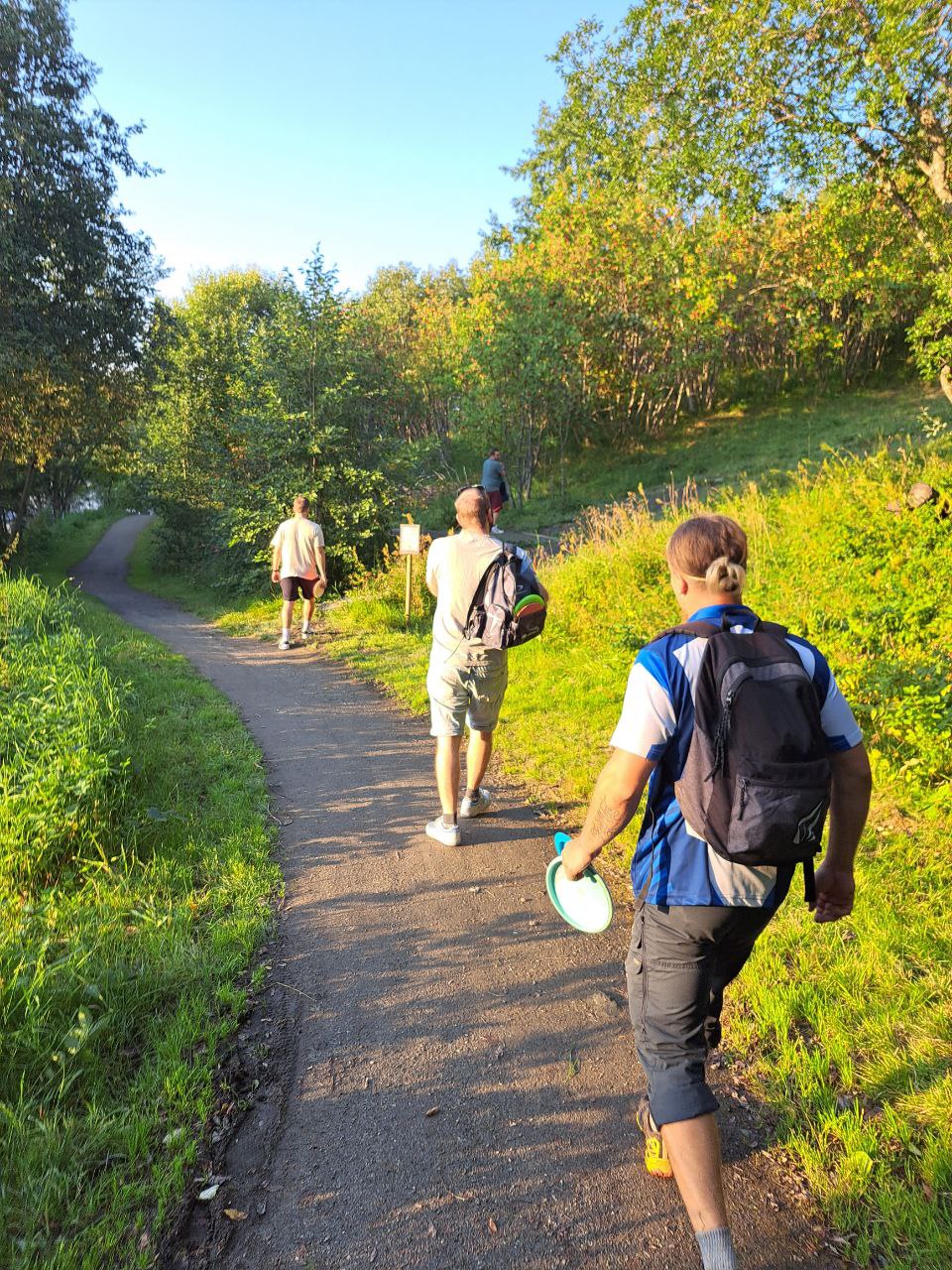 mennesker på tur på sti i skogen, noen med sekk på ryggen
