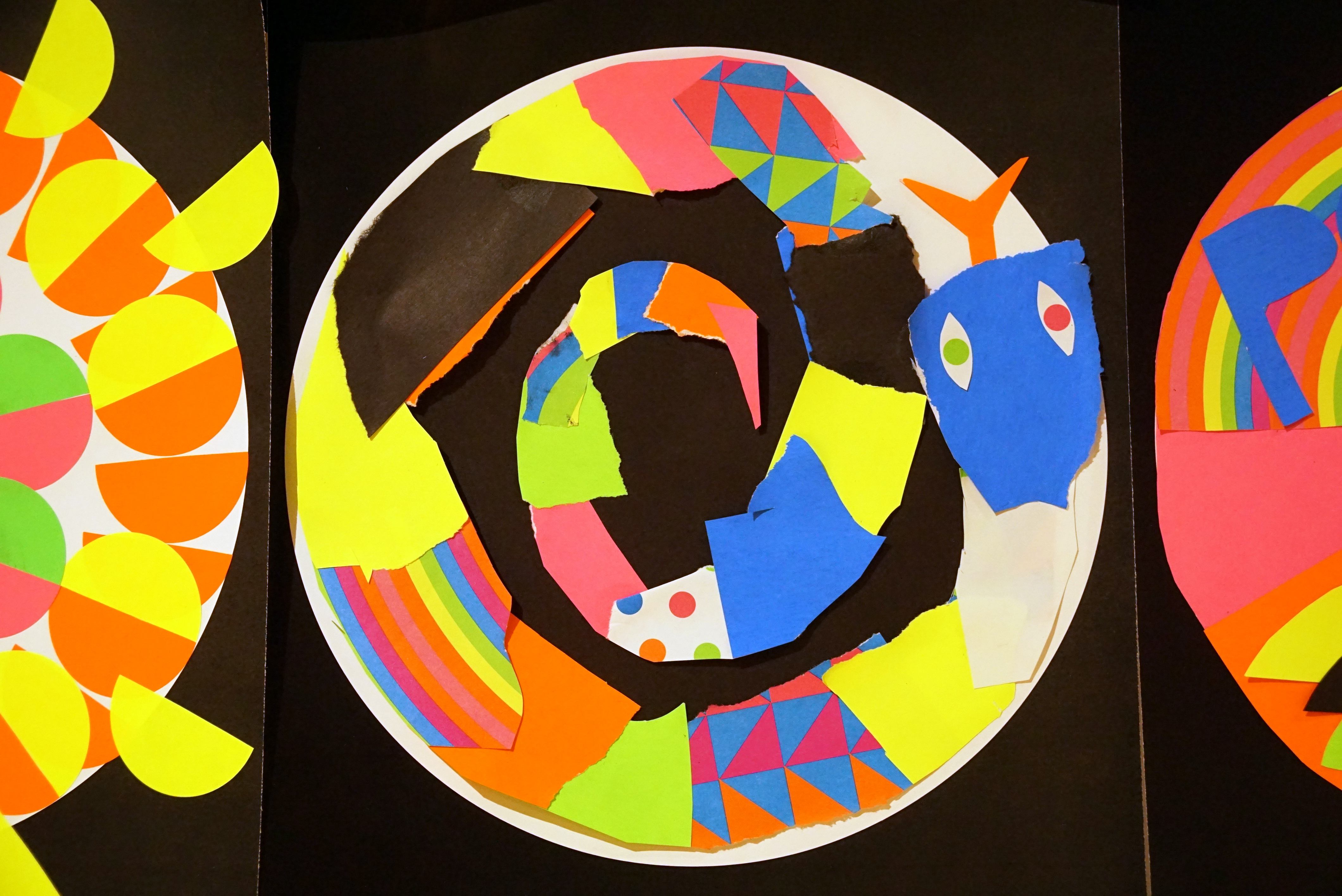 Cut-outs from different colored paper creating a snake curled up in a circle.