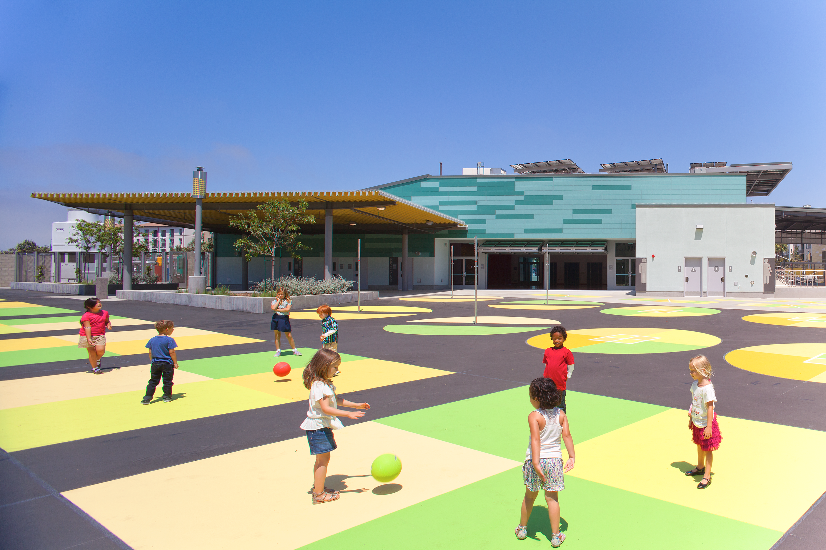 Bright, vibrant geometric graphics on the outdoor area floors, with kids playing with each other.