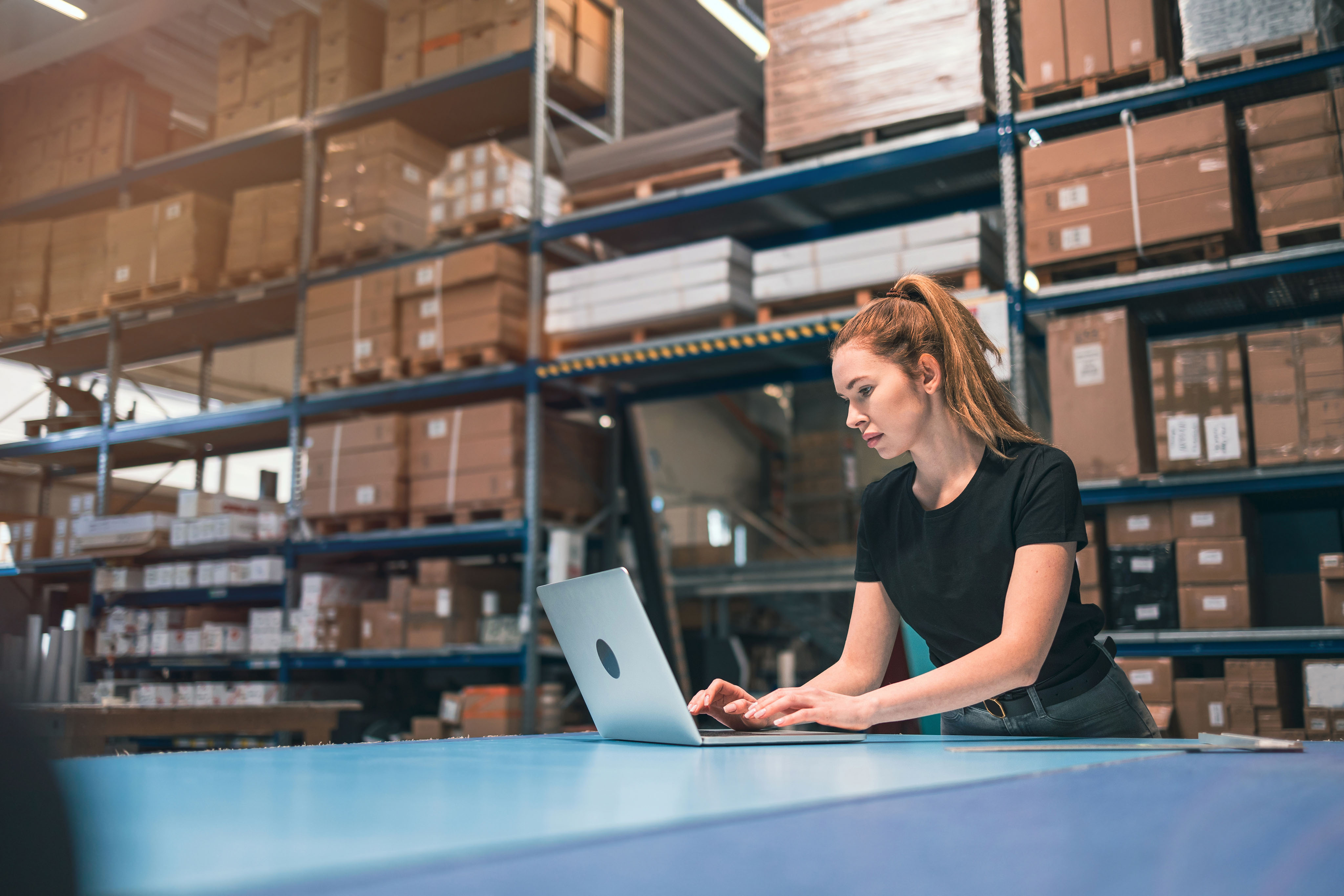 COFOMO – Specialized firm in digital transformation and artificial intelligence for the retail industry – Young woman working on a laptop in a distribution center.
