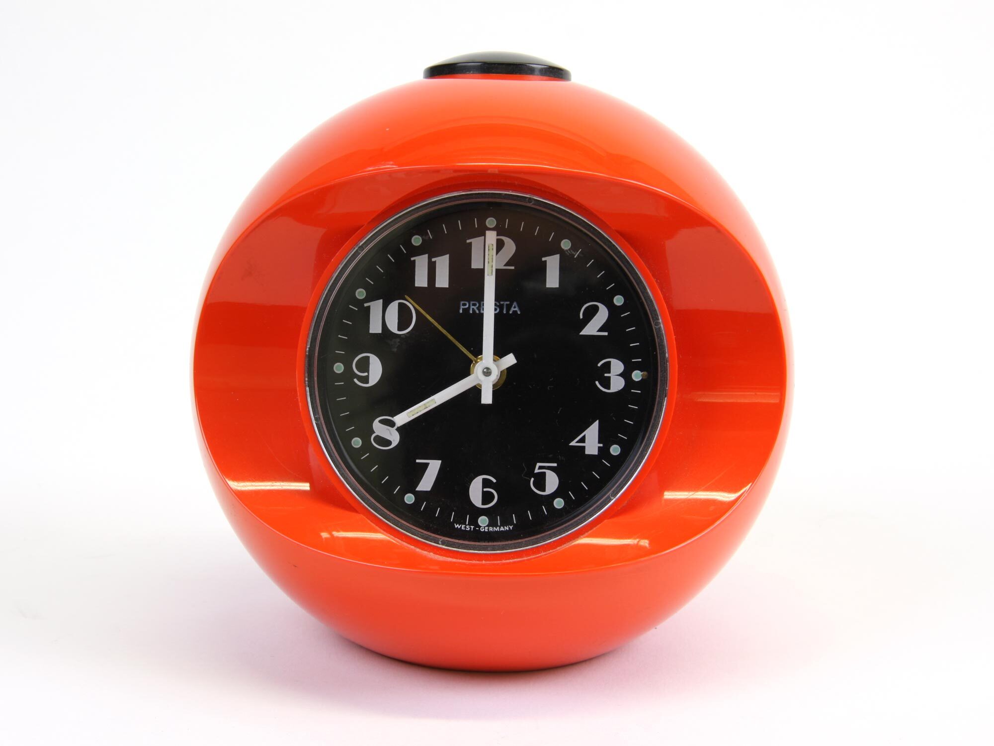 Orange spherical alarm clock with black face and white numerals, showing approximately 12:30, with black winding key on top.