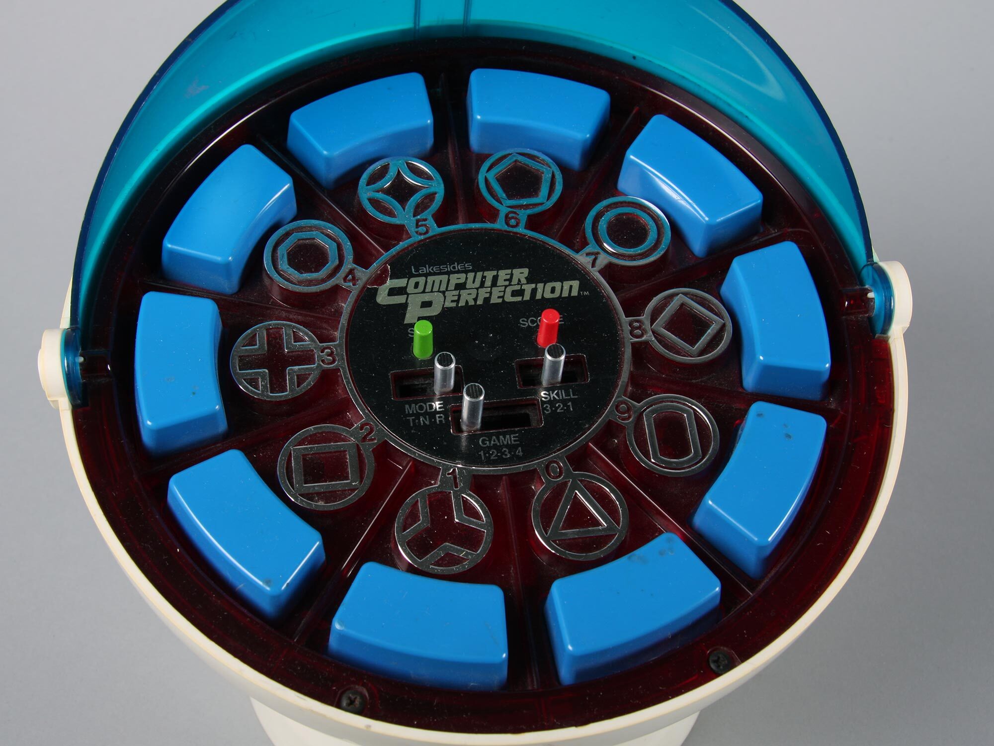 Circular electronic toy with blue plastic segments around edge, dark red centre displaying game symbols and "Computer Perfection" text.