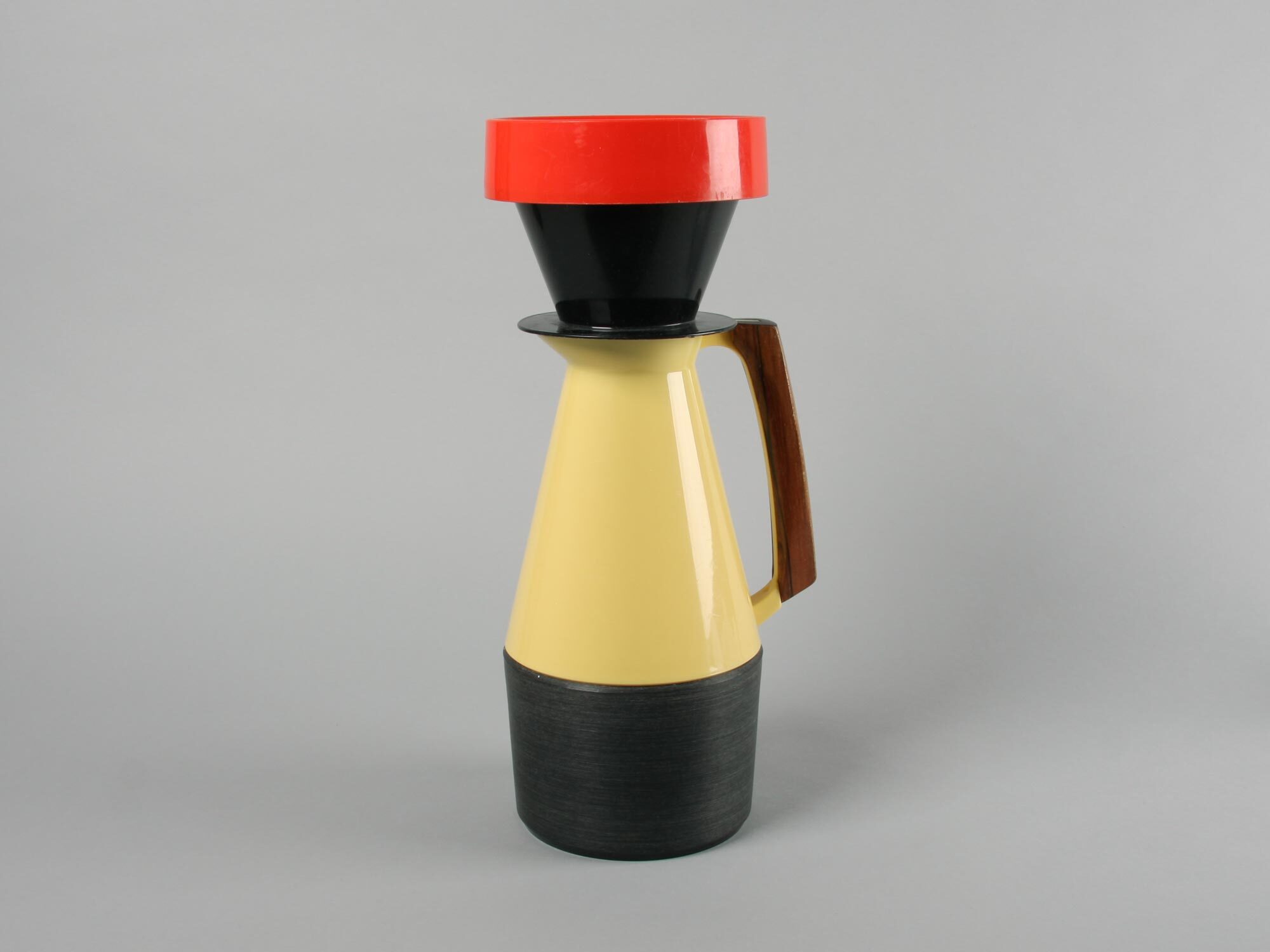 Yellow and black coffee pot with red lid and brown handle on grey background.