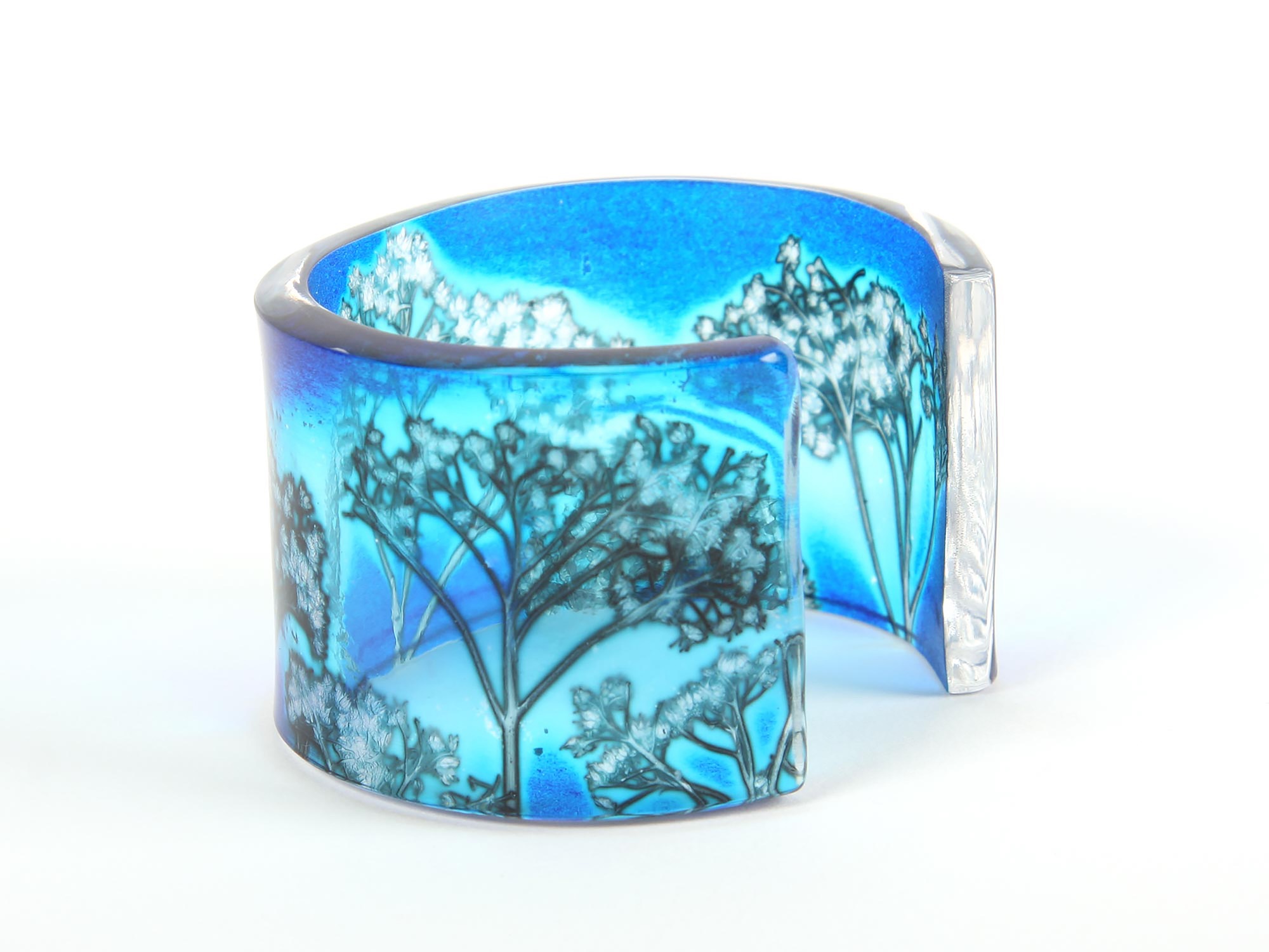 A blue glass cuff bracelet with a tree motif, shown on a white background.