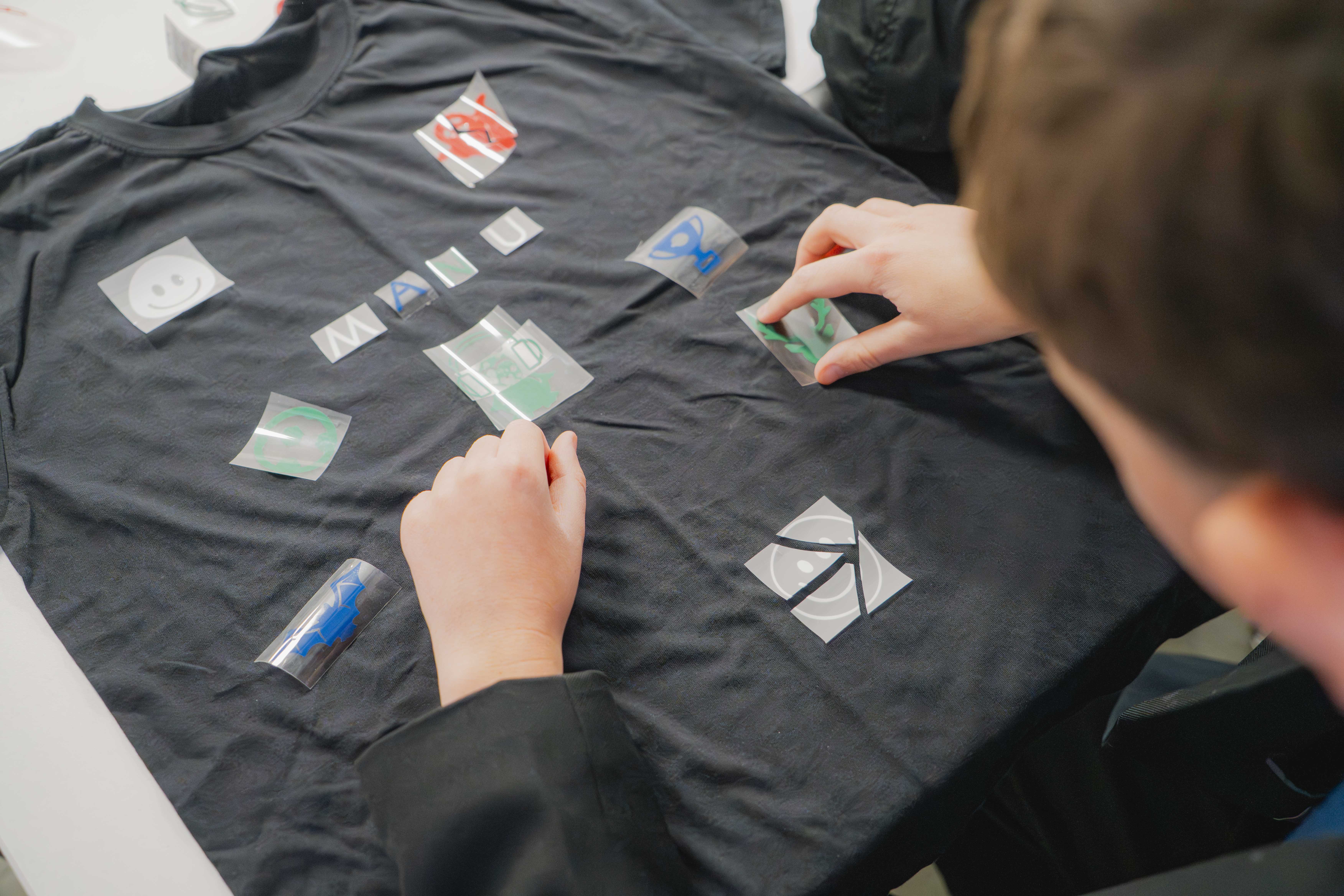 Person sticking symbols and letters in blue, white, green and red onto a black t-shirt.