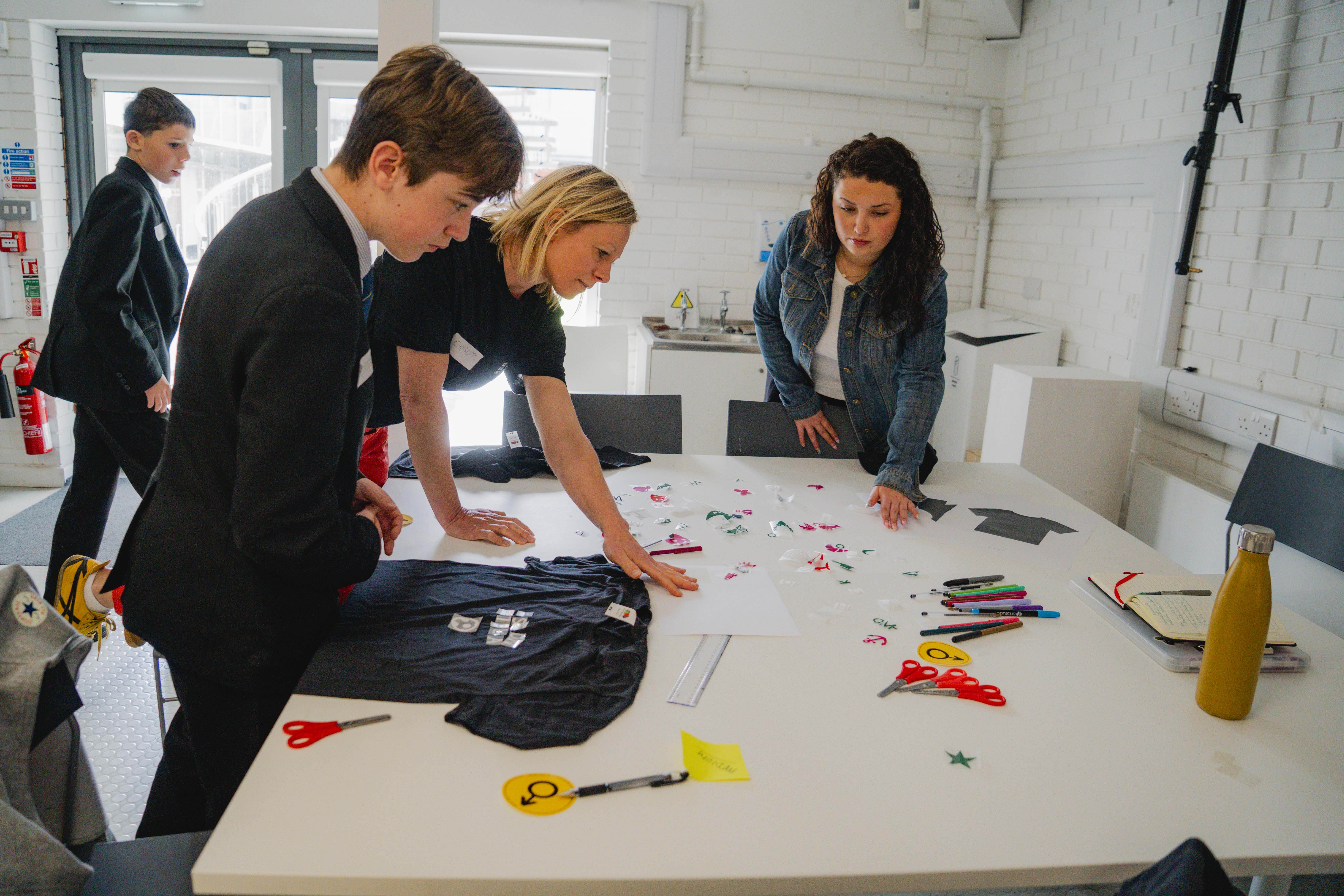 Teachers and students surrounding a table with red and green cutout symbols, white wall.