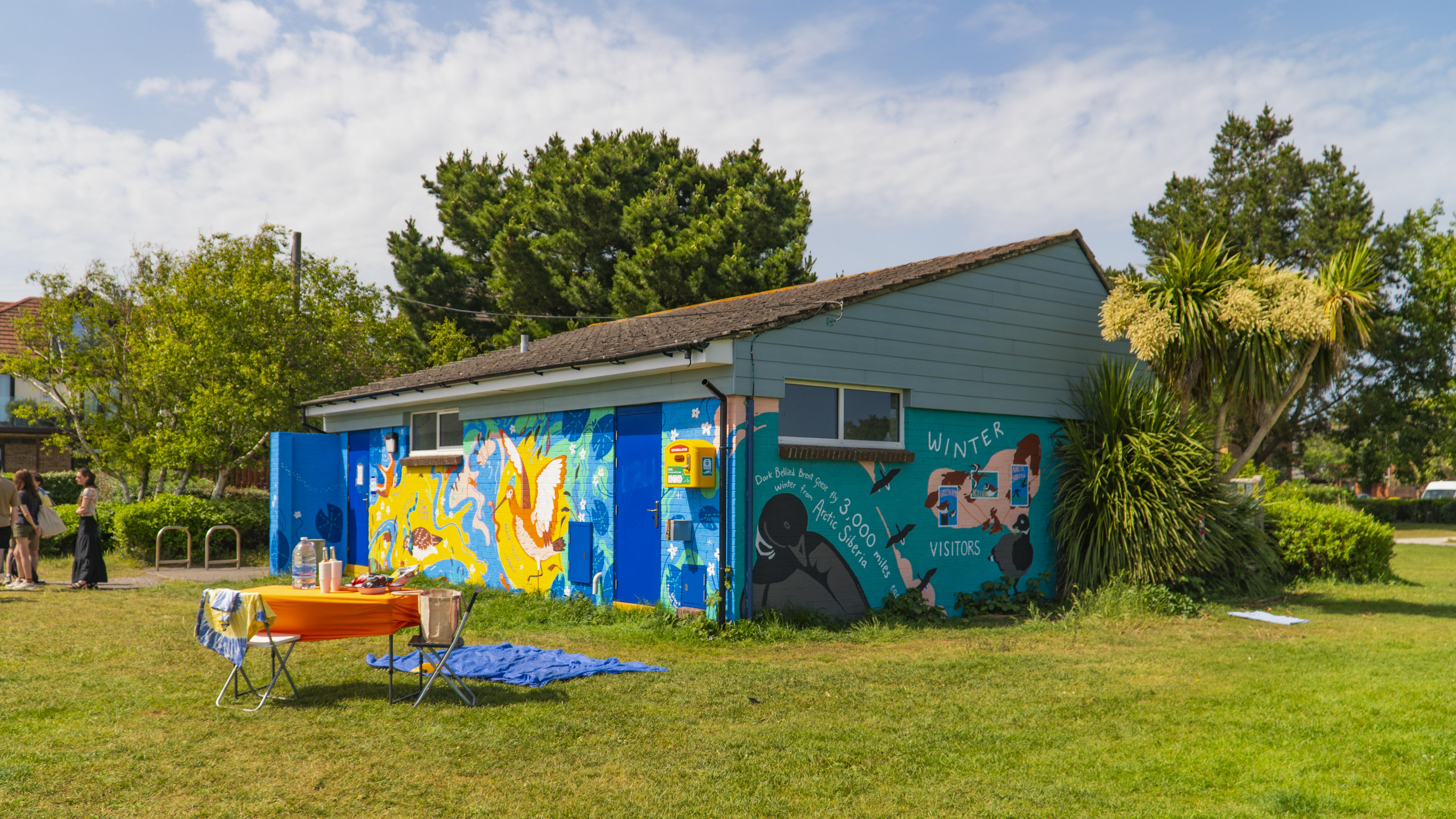 A toilet block building in Baiter Park, Poole, with a bold, colourful mural on its exterior.