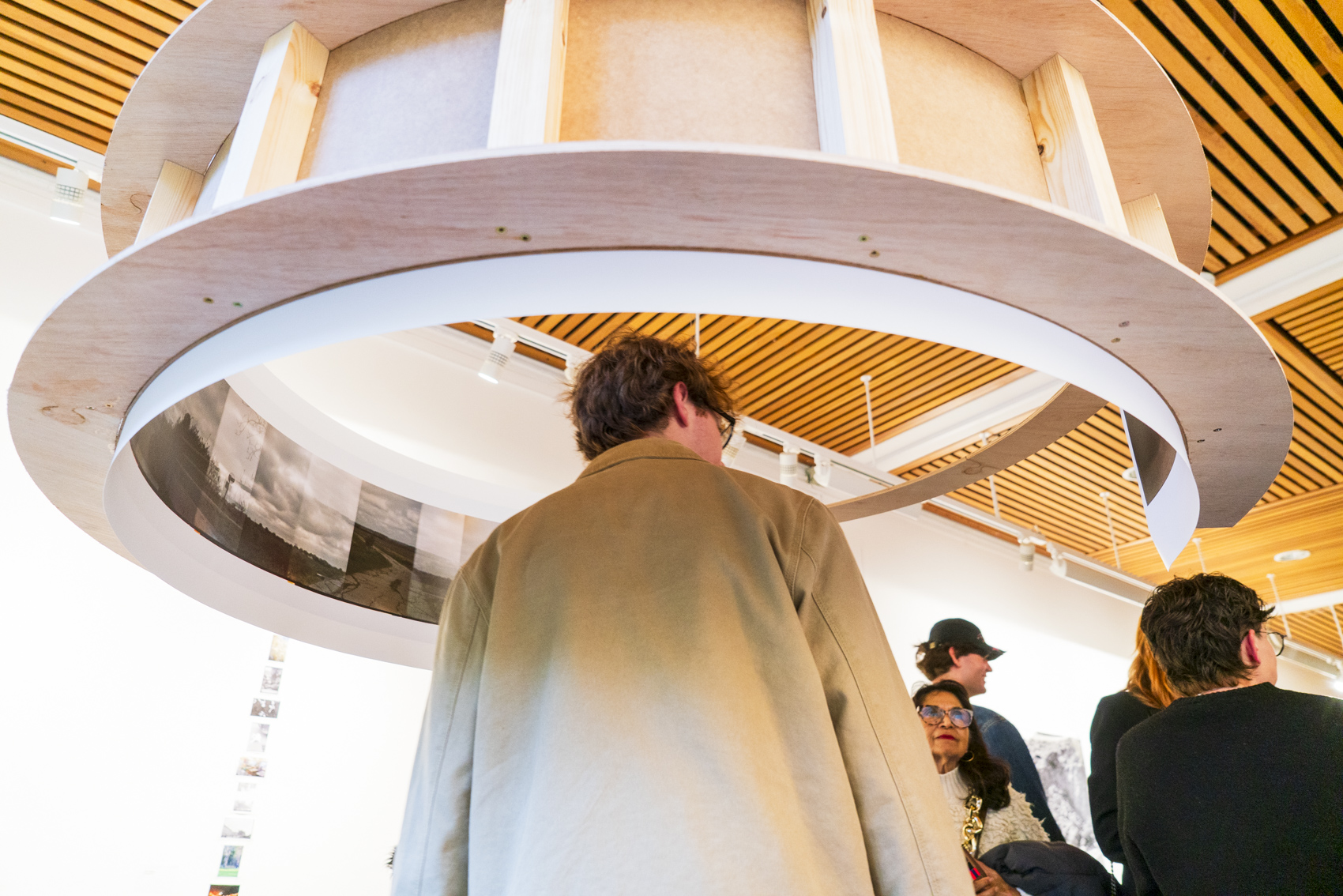 A group of people stands beneath a large circular wooden ceiling feature in a bright interior space.
