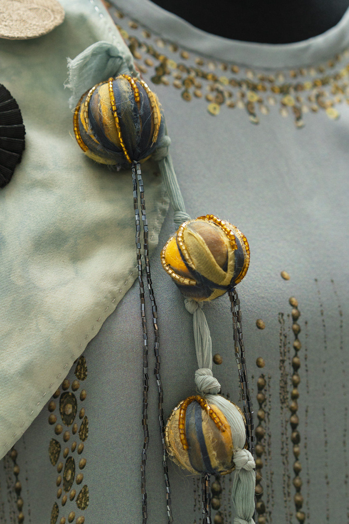 Close-up of duck egg-coloured dress with detailed, golden fabric ball decorations.