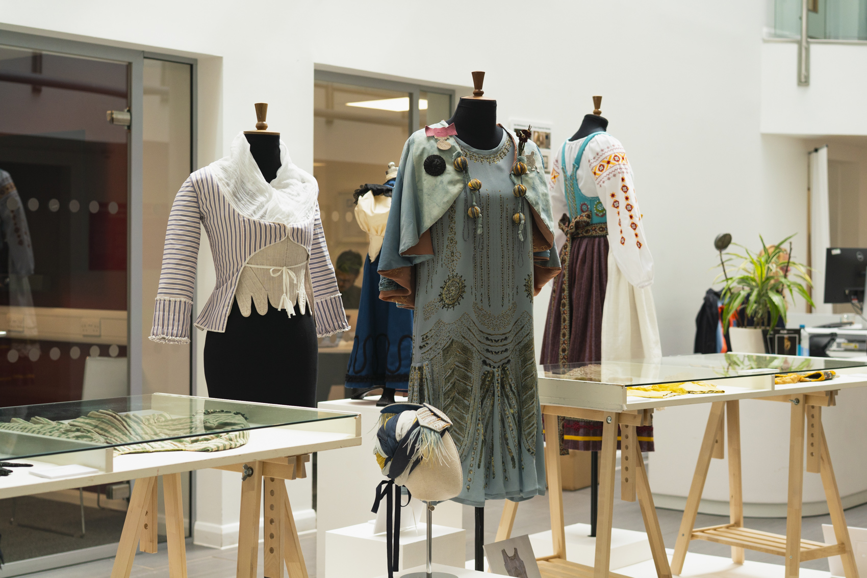 Detailed, ornate garments on display with wooden display tables.