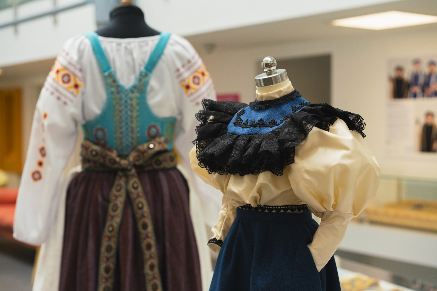 Two detailed historical dress garments on display, one with black and blue ruffles, the other with detailed red-gold patterning.