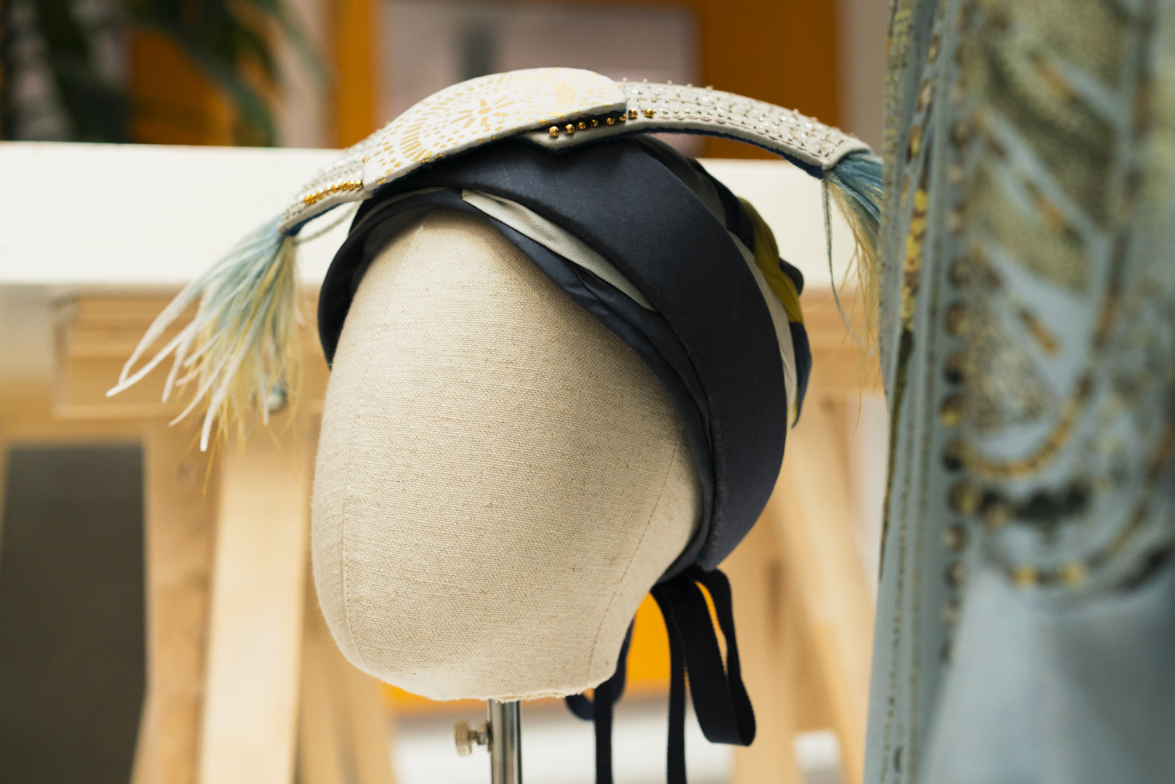 Mannequin head wearing black headpiece with gold sequins and feathers.