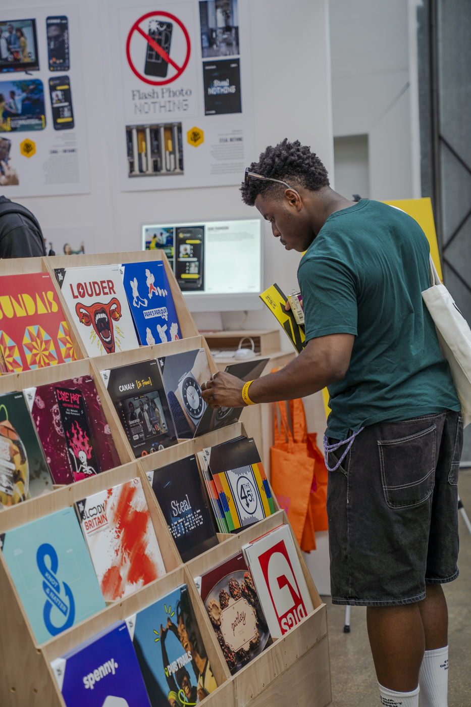 A person in a green T-shirt browses vinyl records in a shop, standing beside a wooden display rack with colourful album covers.
